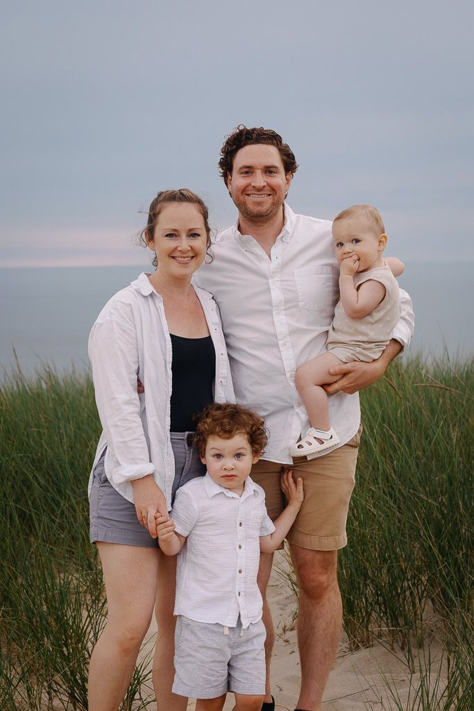 A family poses together on a sandy beach with tall grass in the background during sunset.