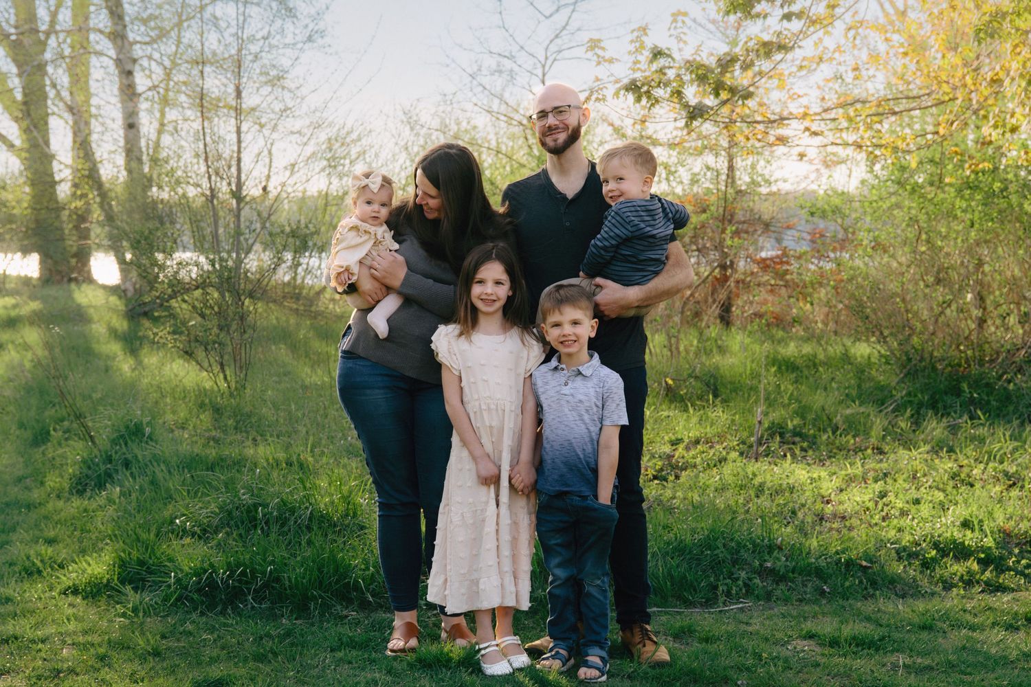Happy family of five posing outdoors in a lush green park during golden hour spring evening.