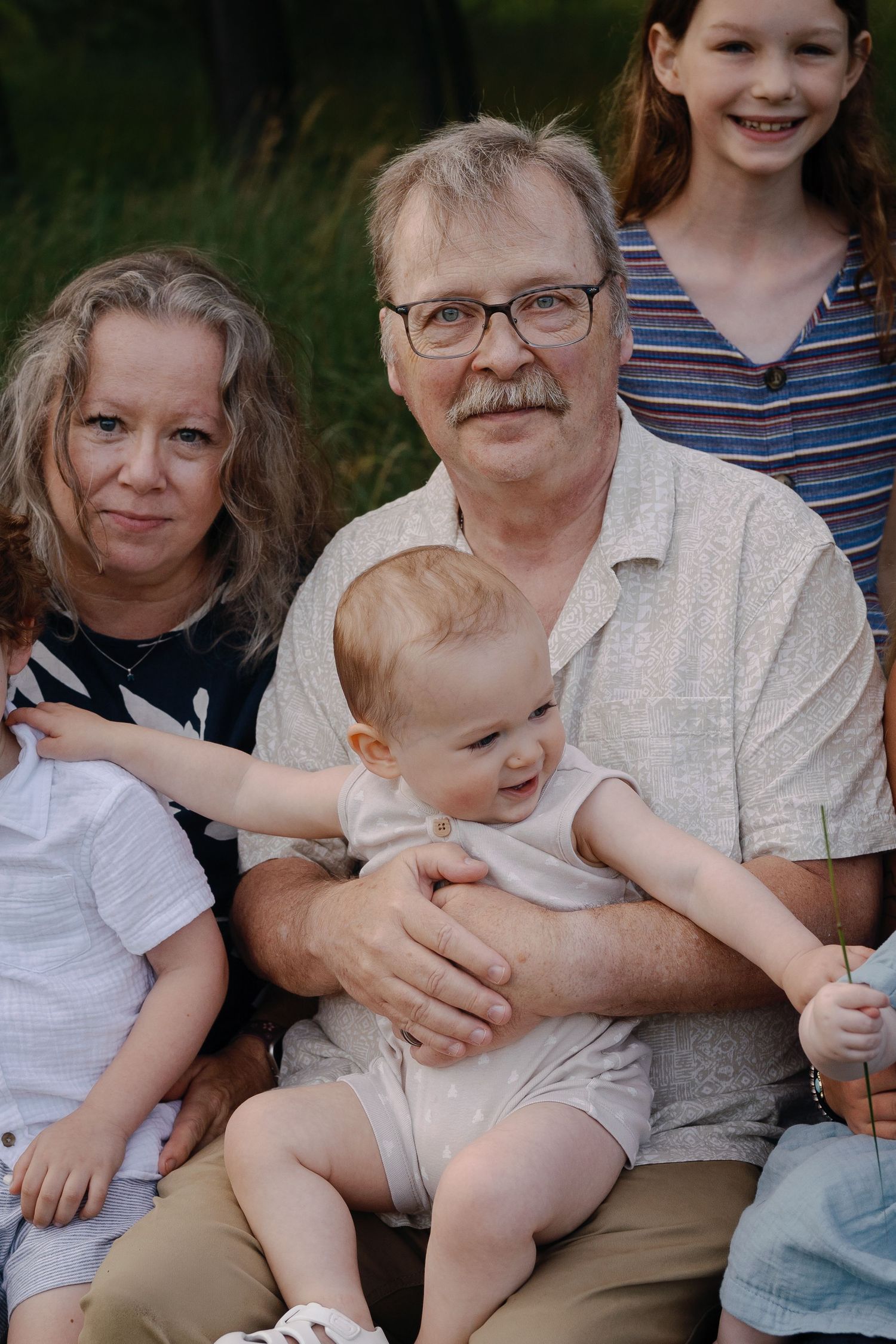 Extended family members share a tender moment together on a bench in an outdoor setting.