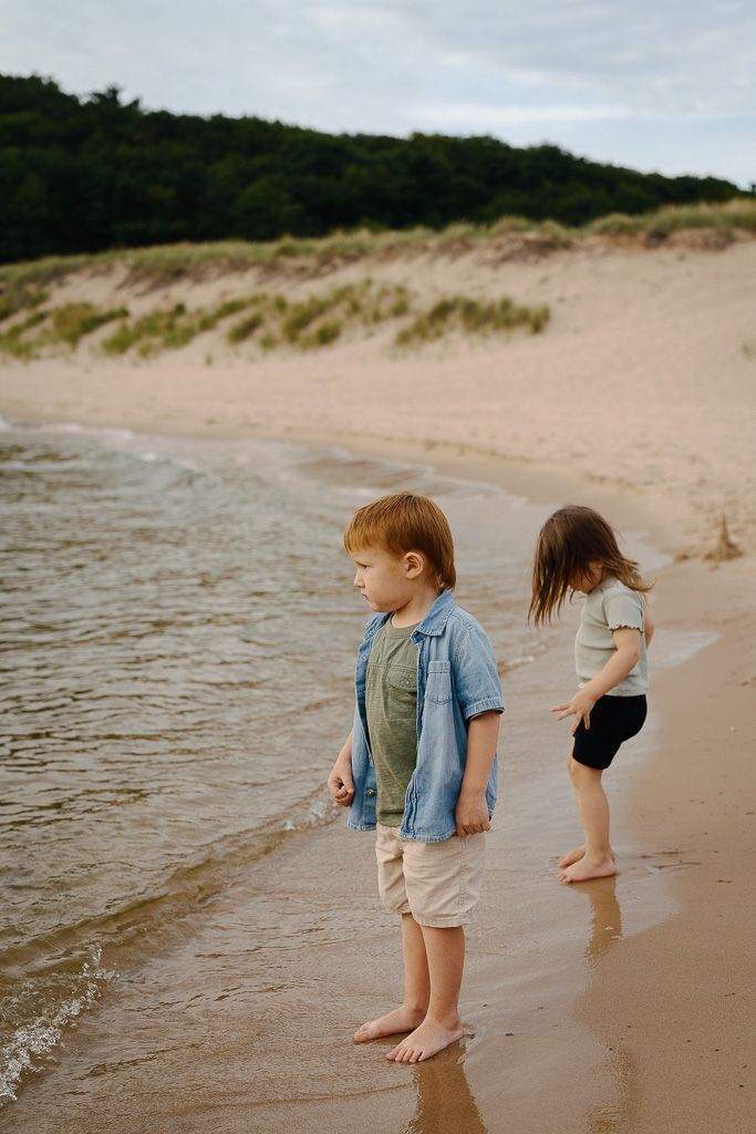 Two children playing and splashing at the water's edge on a sandy beach during a summer day.