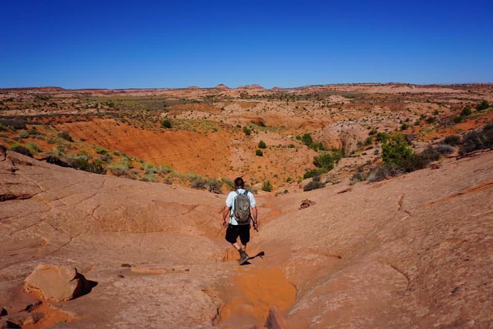 Desert landscape with red rock formations and hiking trails under bright blue sky.