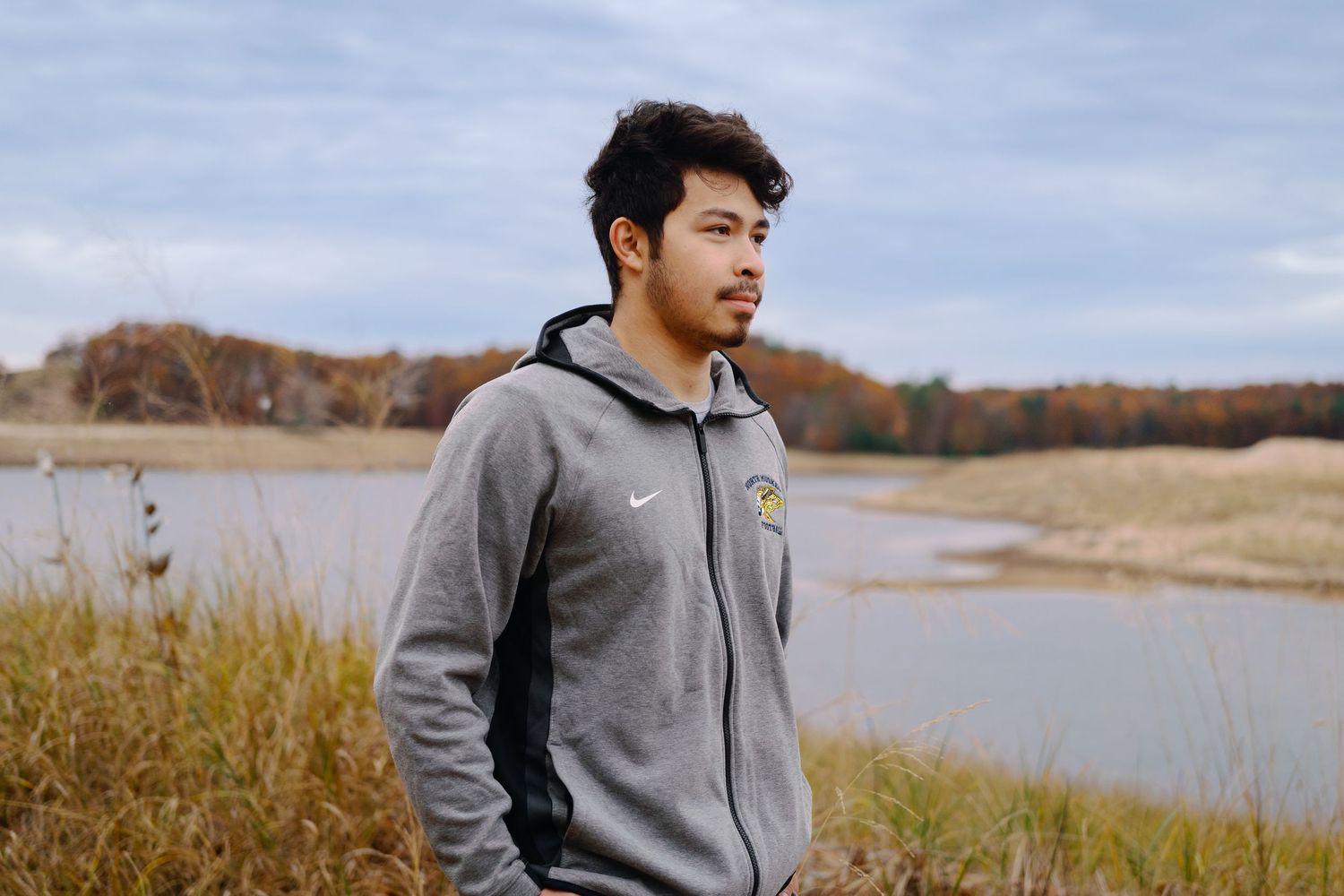 Person in grey hoodie photographed against autumn lakeside scenery.