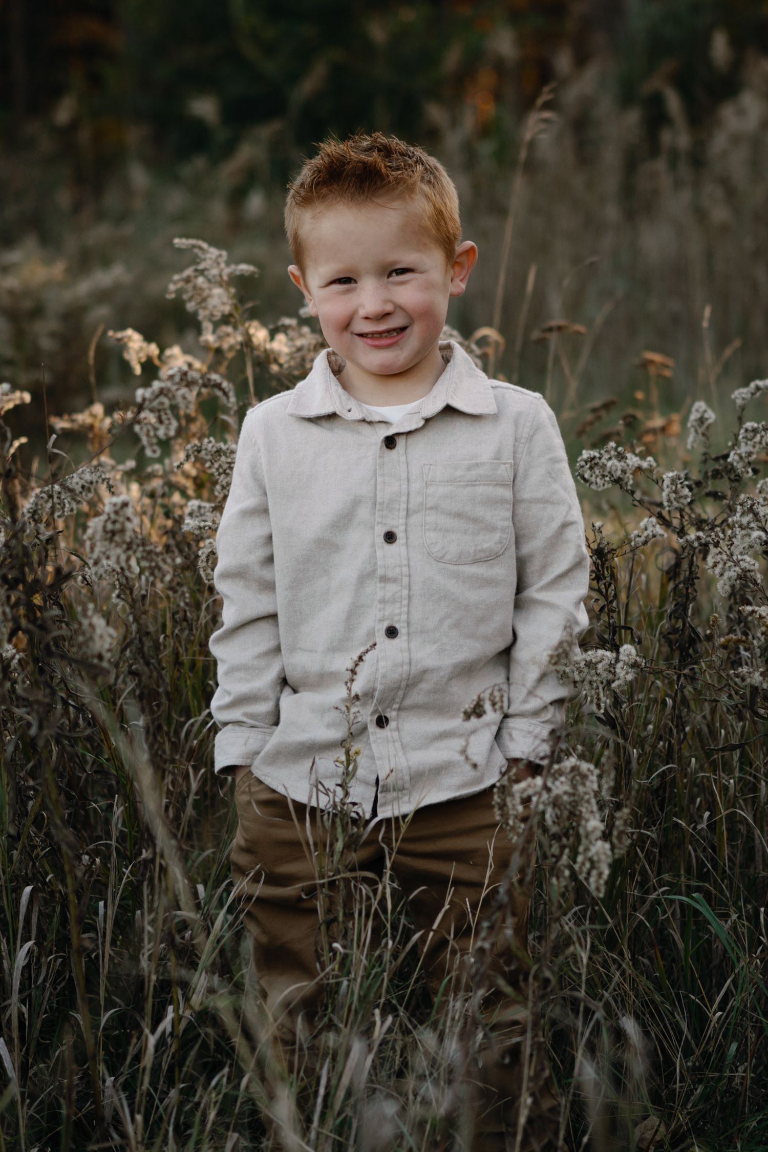 A child poses cheerfully among tall dried grasses in casual autumn attire.