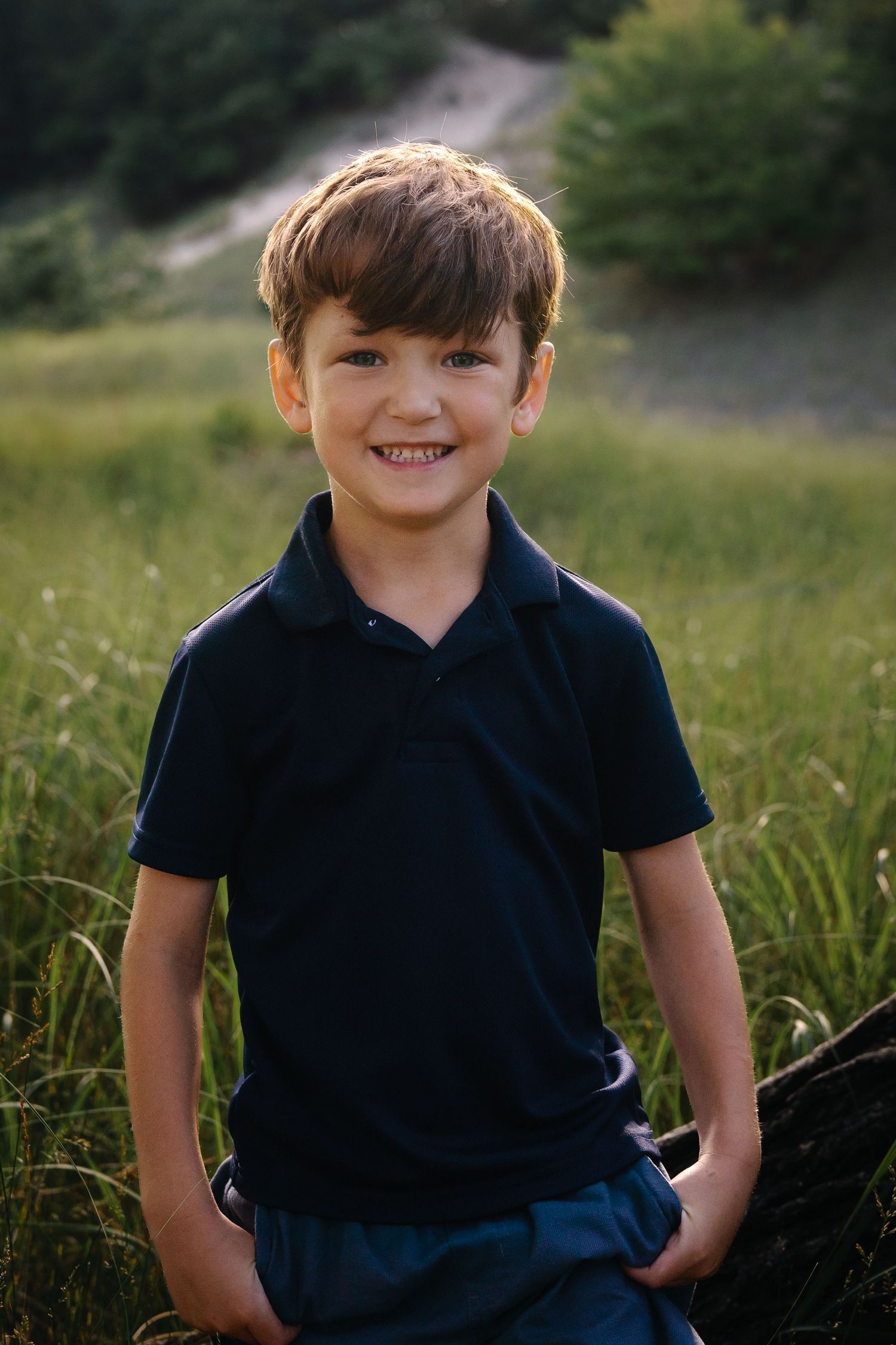Child wearing navy polo shirt poses playfully in outdoor setting.