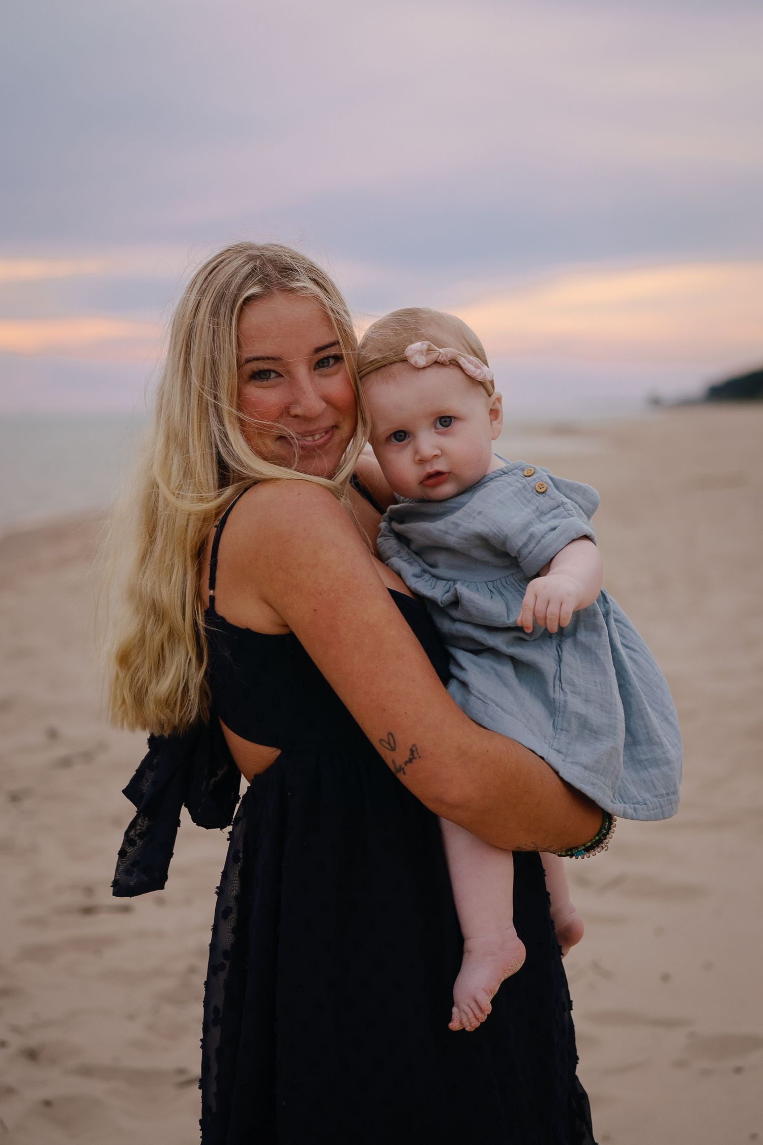 Mother and baby share tender moments on a sandy beach at sunset.