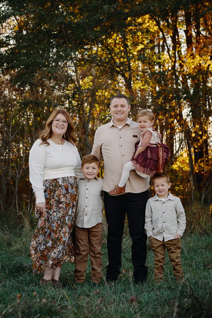 A family poses together in a grassy field during golden hour with autumn trees in the background.
