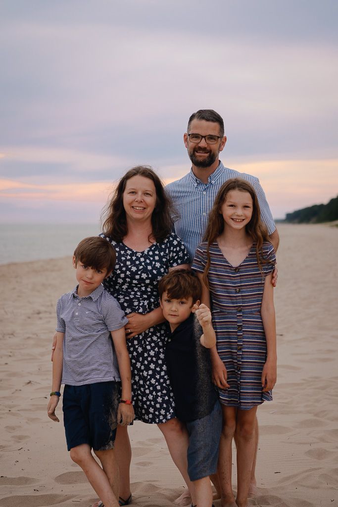Family portrait at sunset on a peaceful beach with ocean and cloudy sky in the background.