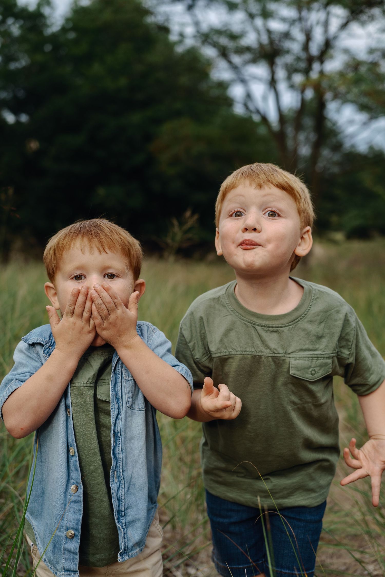 Children in casual clothes making silly faces while playing outdoors in a grassy field.