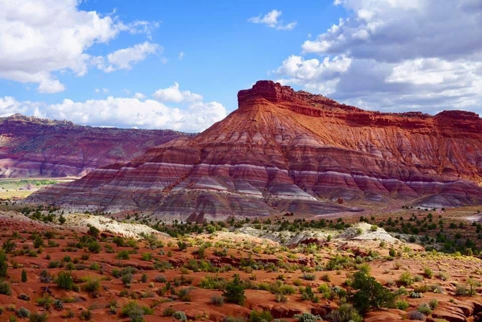 Panoramic view of colorful desert cliffs and mountains under blue sky with white clouds.