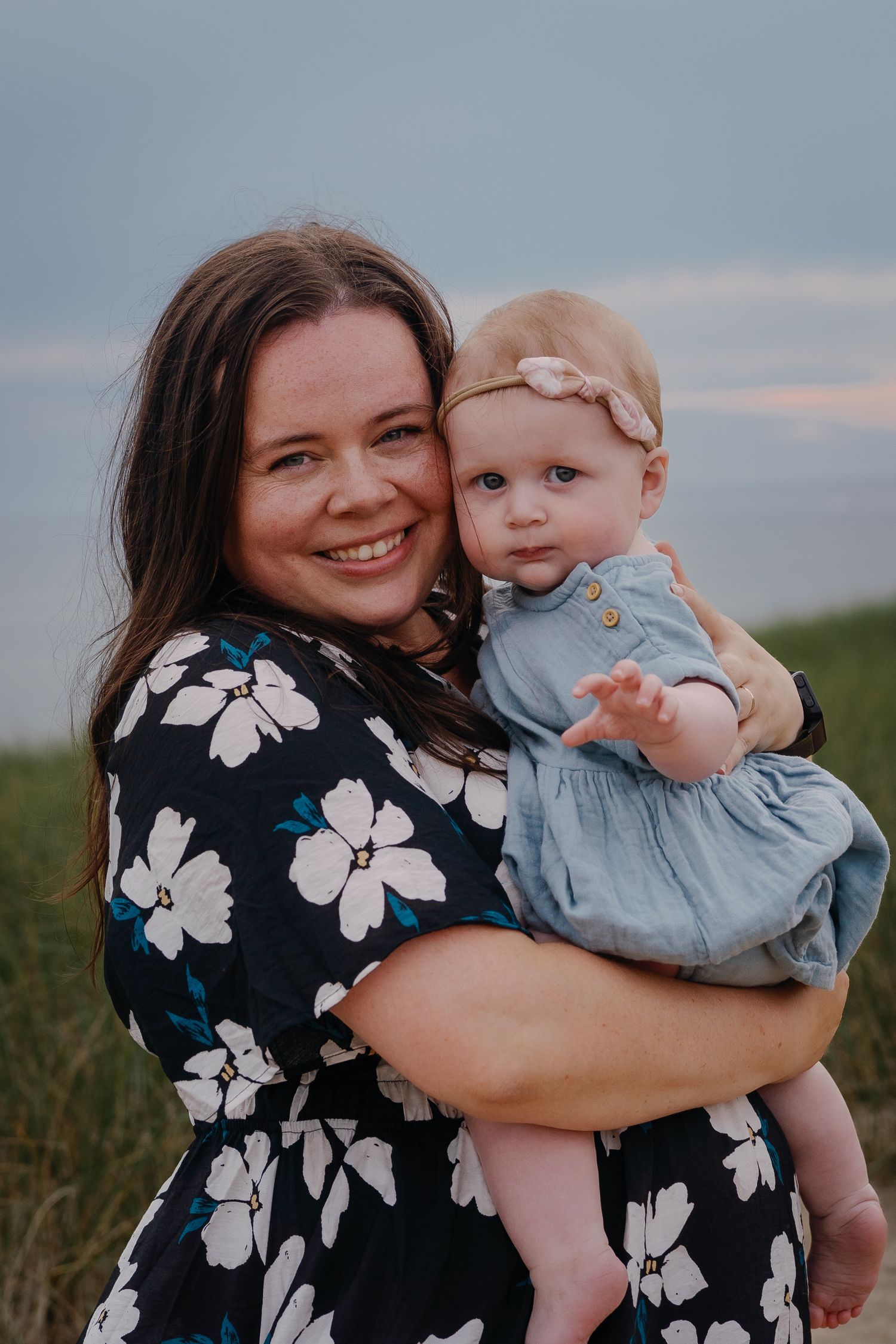 A mother and baby share tender moments in a floral dress against a sunset backdrop.