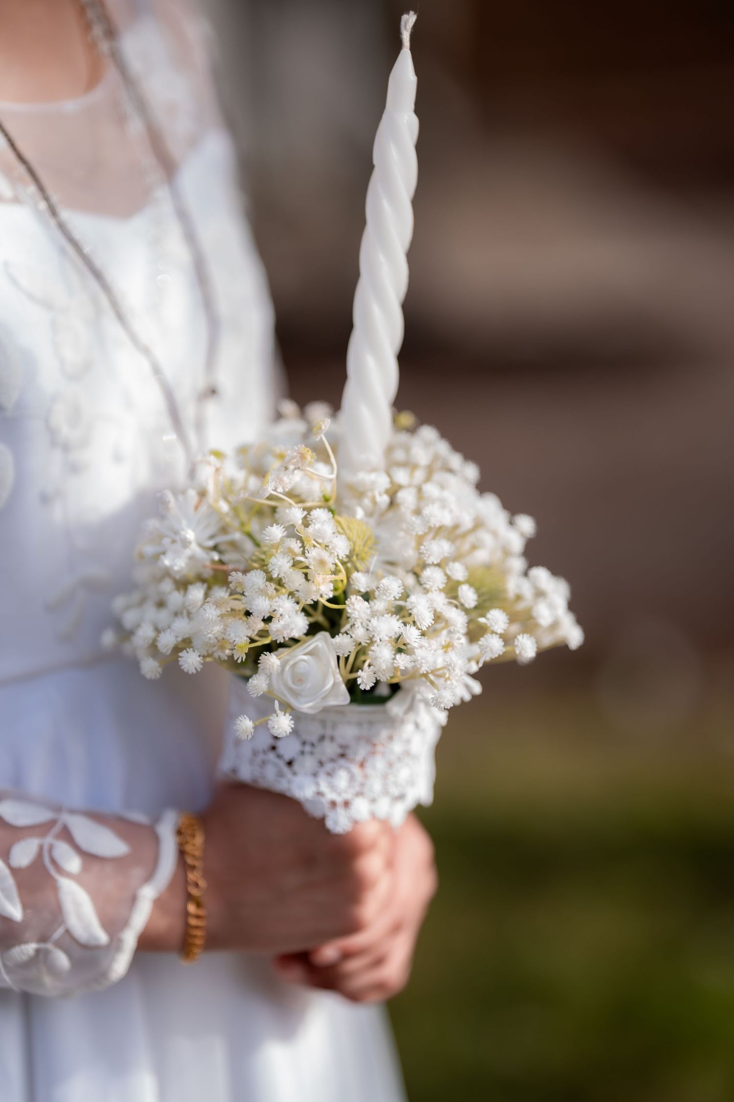 Bride in white lace dress holding elegant bouquet of lily of the valley with twisted white candle.