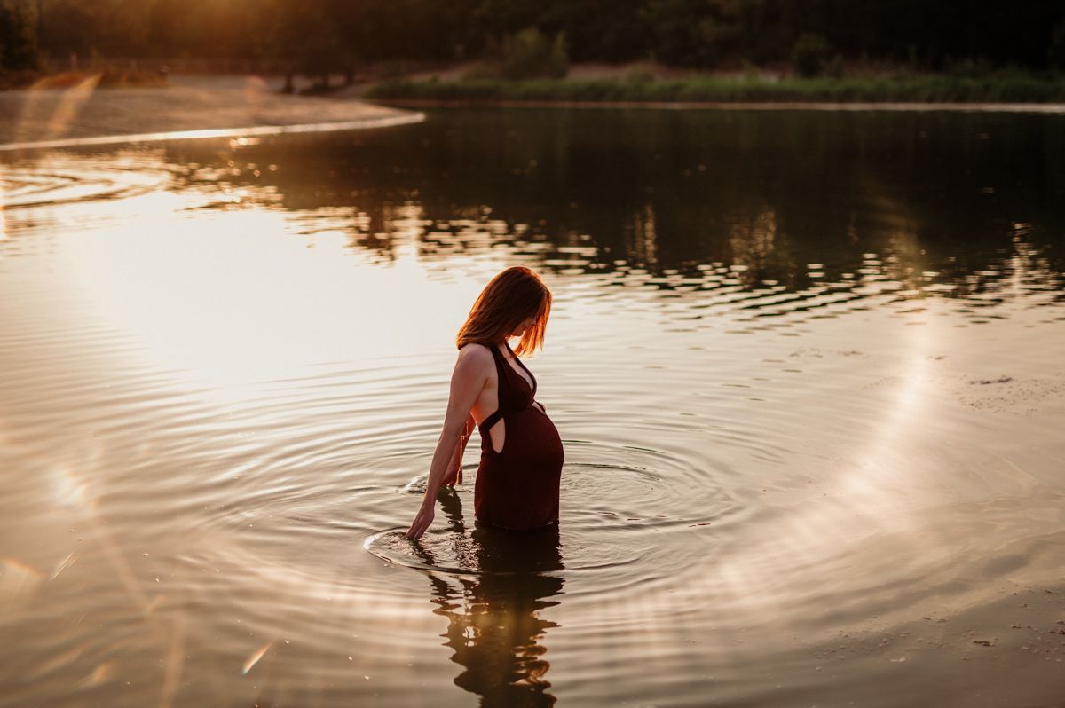Zwangere vrouw tijdens een zwangerschapsshoot in het water op de Bergse Heide tijdens golden hour.