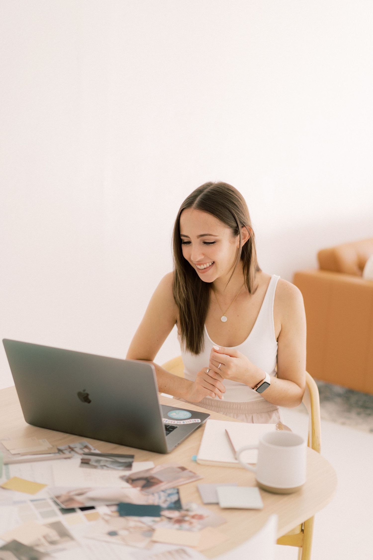 Woman working on laptop at bright minimalist desk with coffee and papers.
