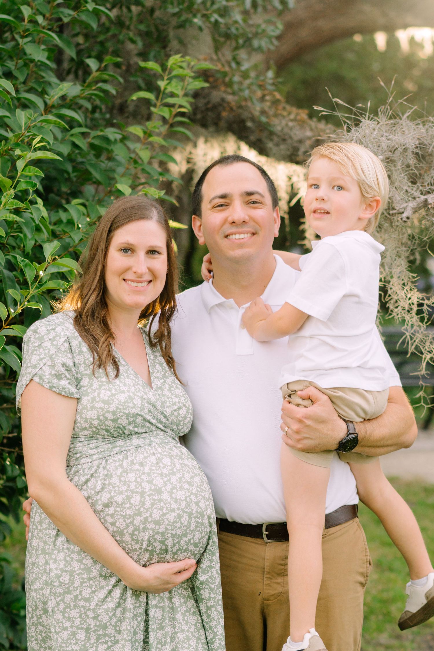 Family portrait in a garden setting with greenery and natural lighting.