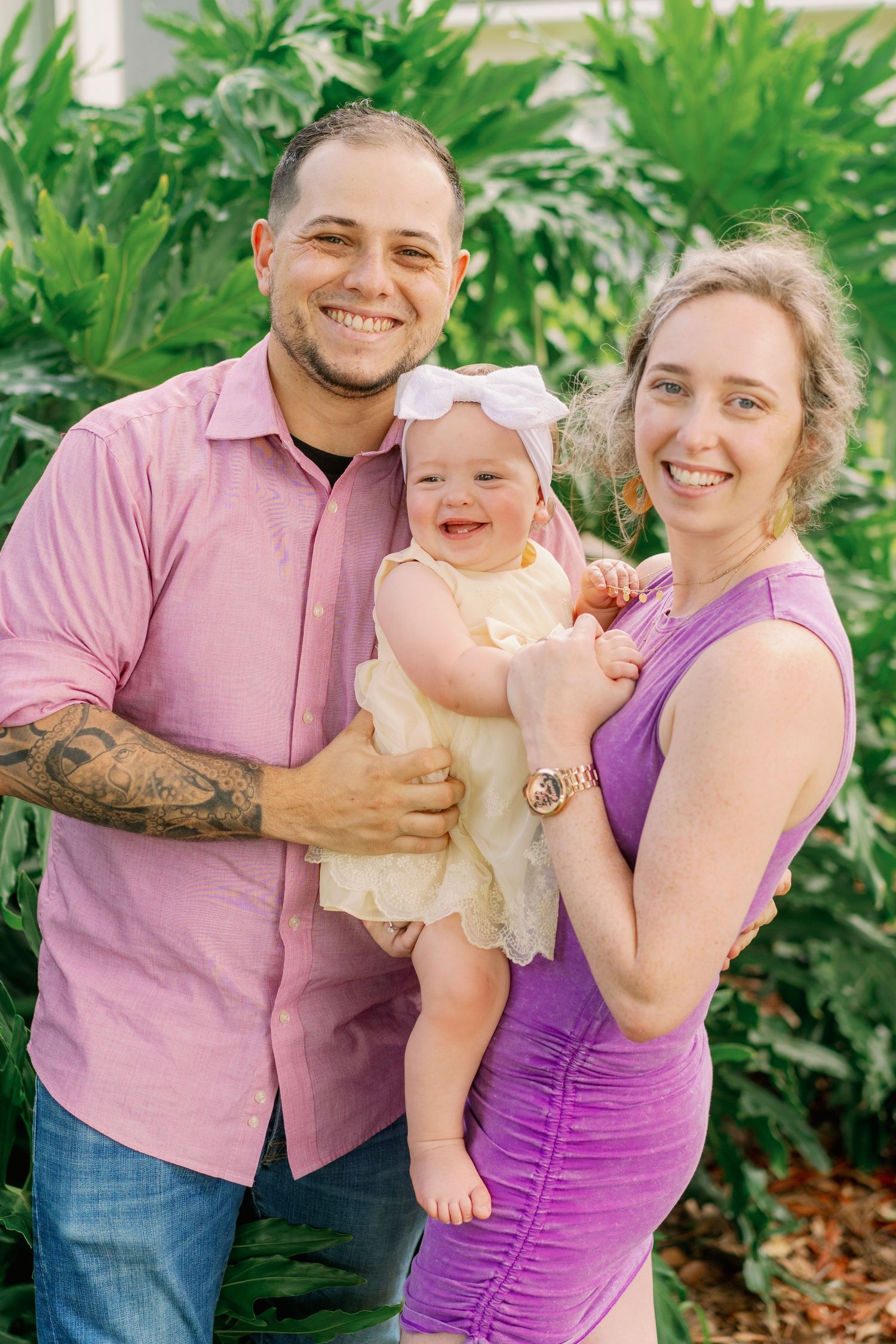 Outdoor family portrait with tropical plants and greenery in background.