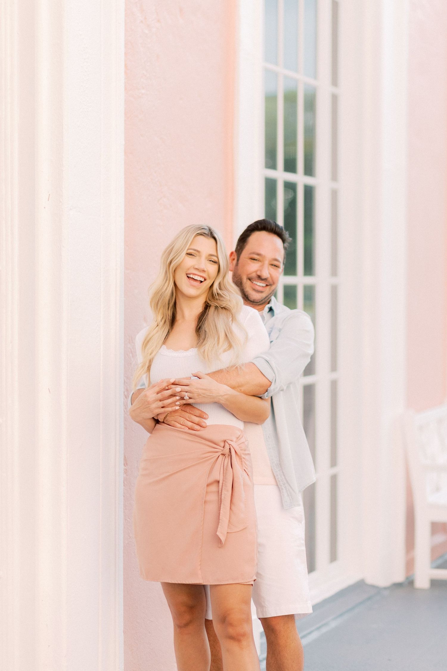 Couple sharing joyful moments together outside pink historic building with white columns.