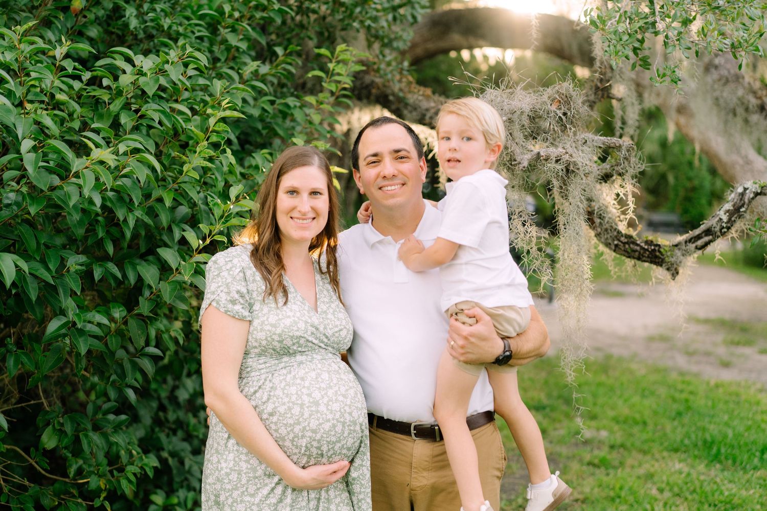 Outdoor family photo with lush green foliage in the background.