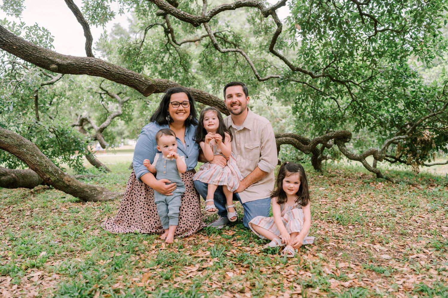 Family sitting together under large oak tree branches in a park.