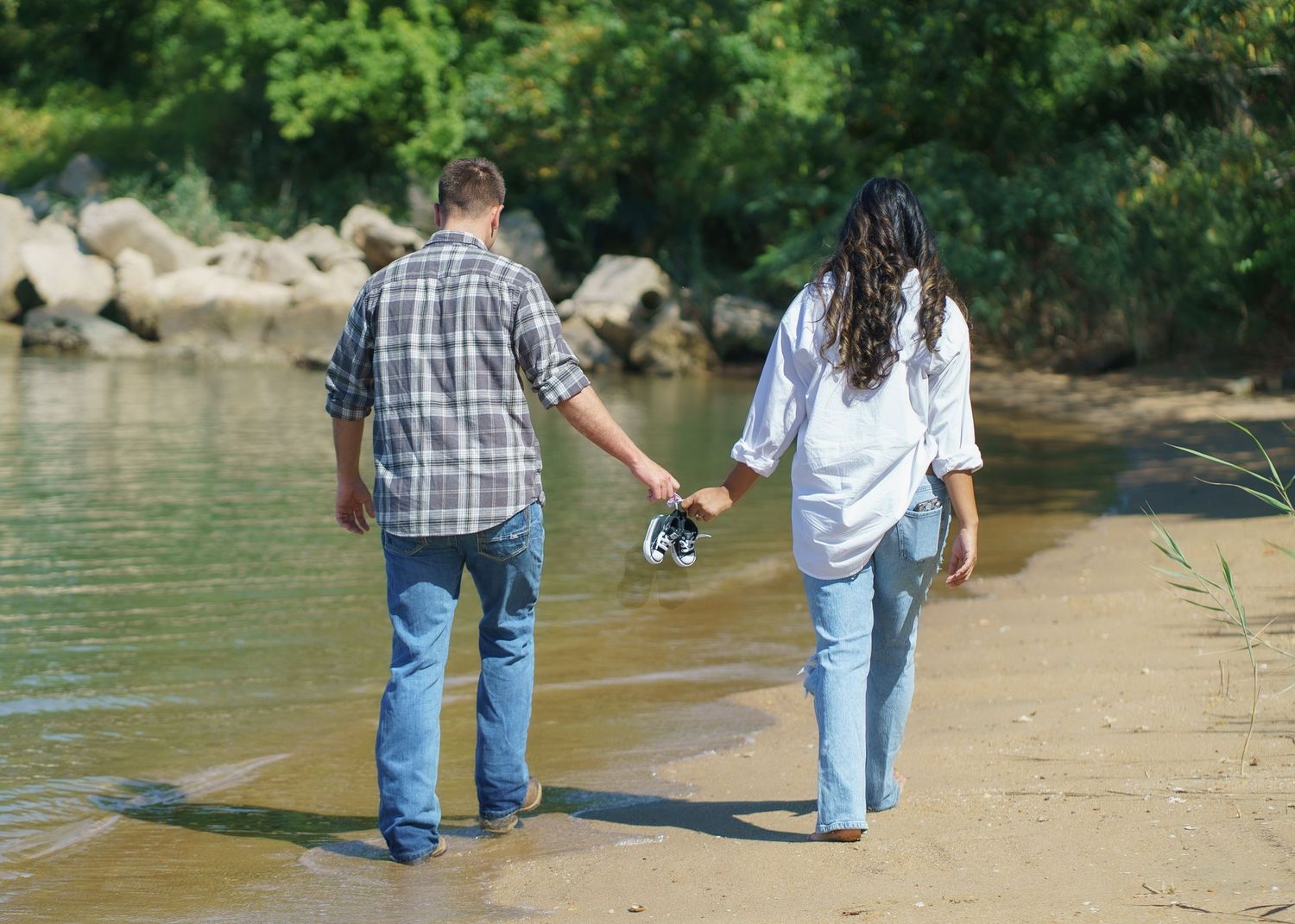 A couple walks along a sandy riverbank during a photo session.