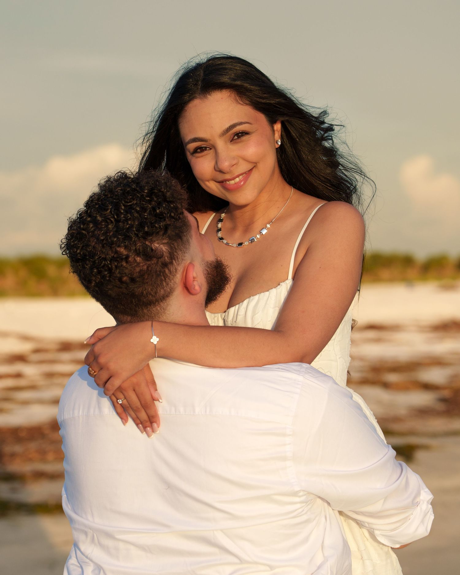 Couple in white clothing sharing intimate moments on sandy beach at dusk.