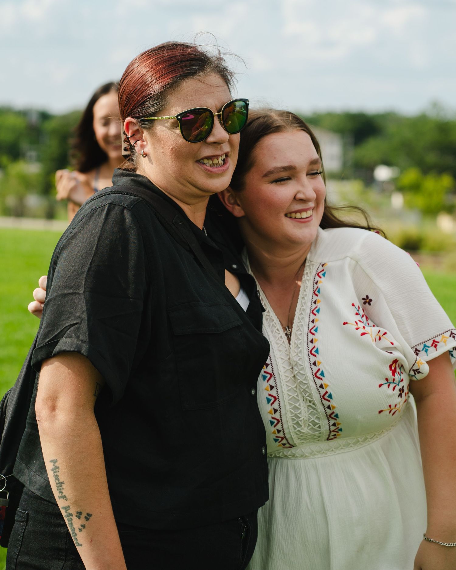 Two people share a joyful moment outdoors on a sunny day in a grassy field.