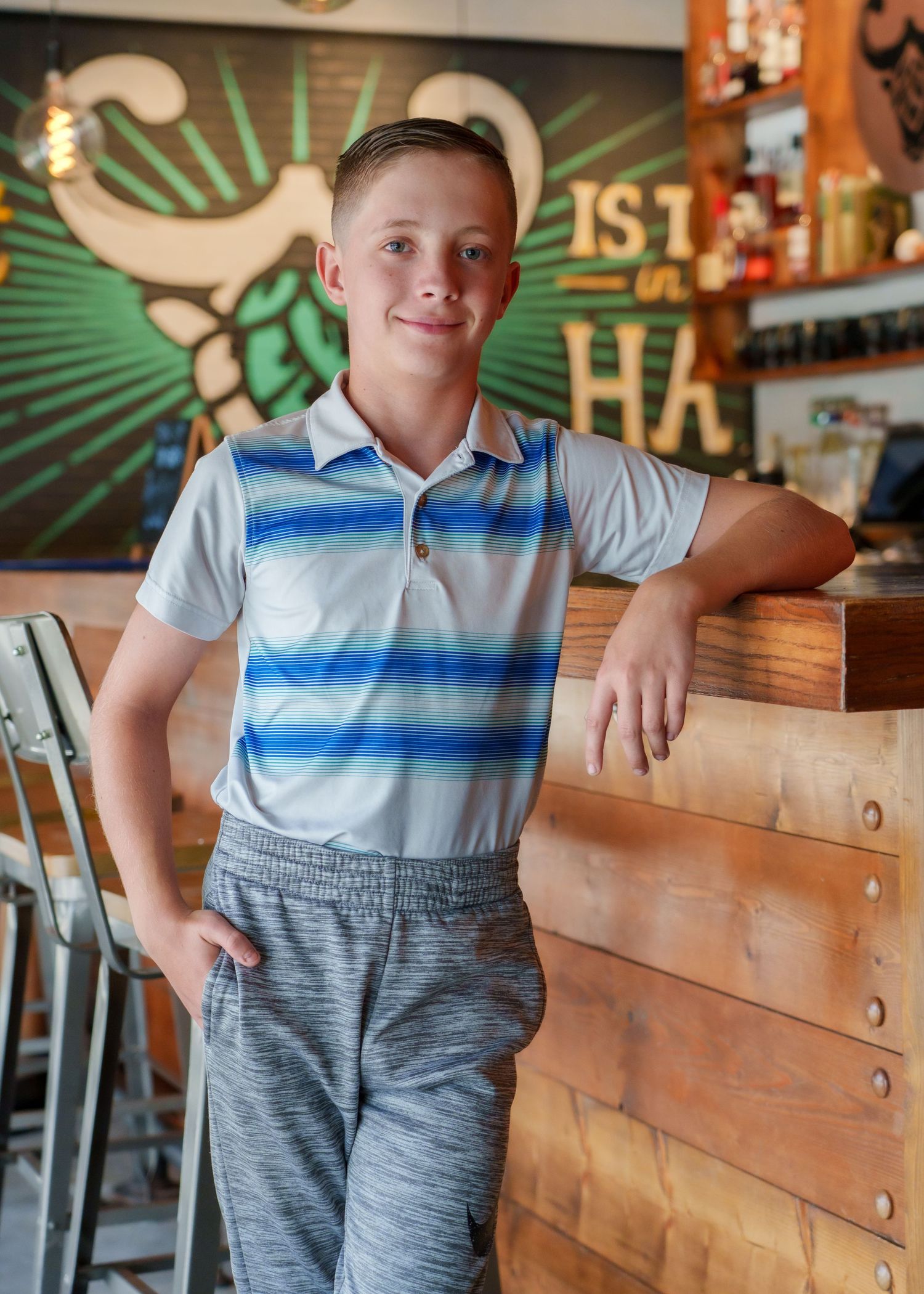Child wearing blue and white striped polo and gray pants posing in restaurant interior.