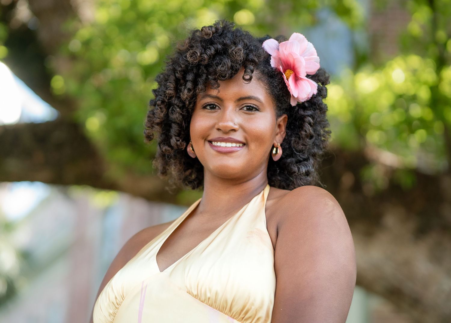 Outdoor portrait series with a pink flower accessory against lush green foliage.
