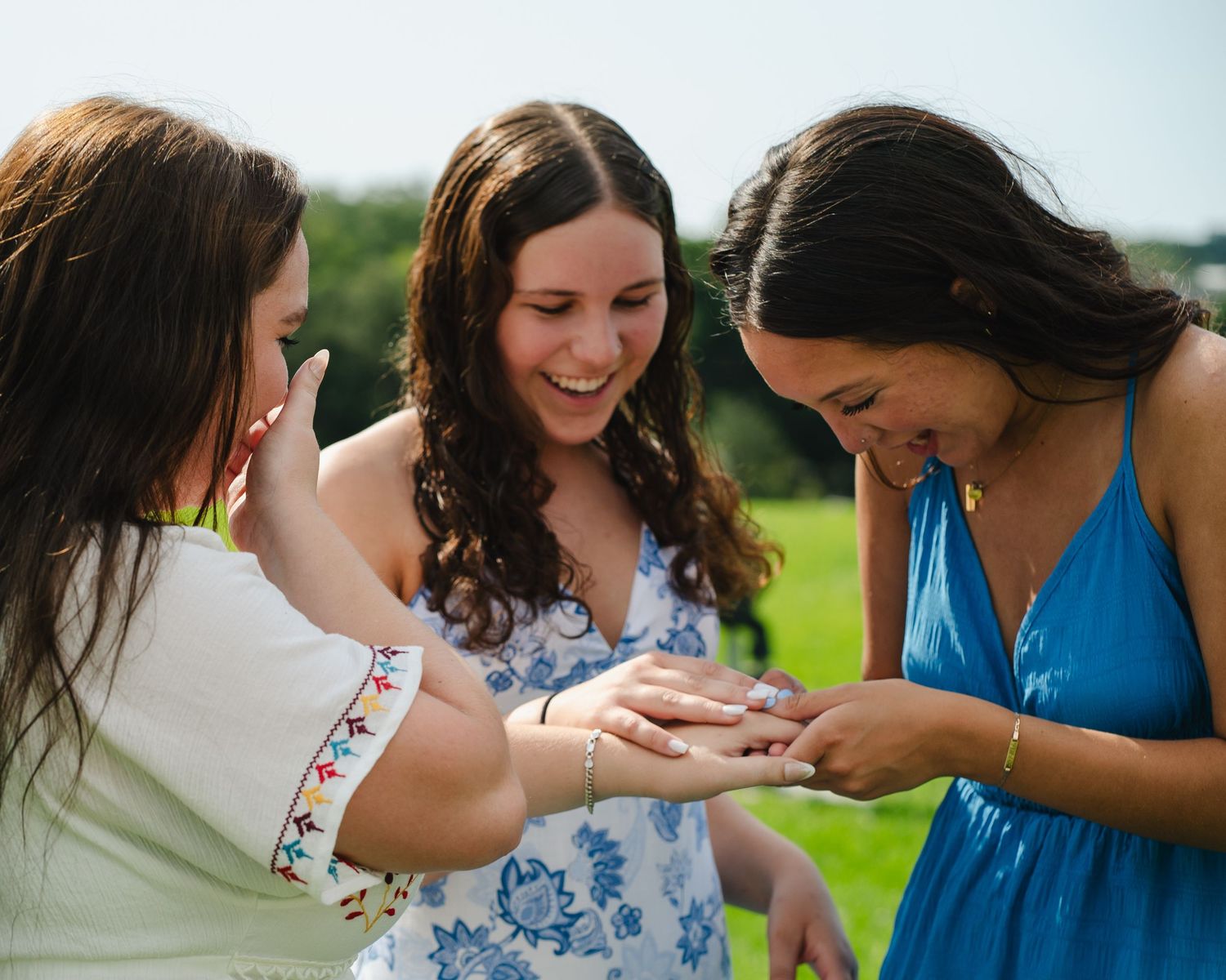 A group of friends laugh together while standing in a lush green field.