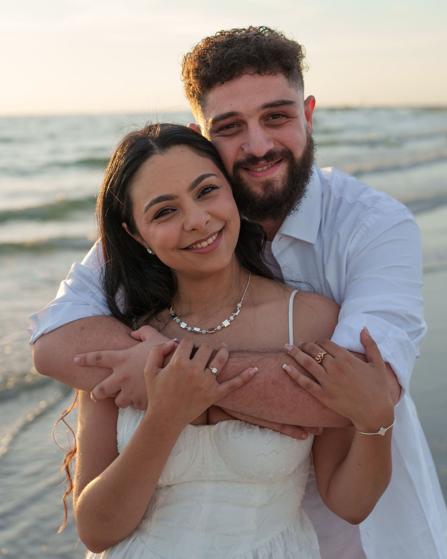 Happy couple embracing and laughing during sunset beach photoshoot.
