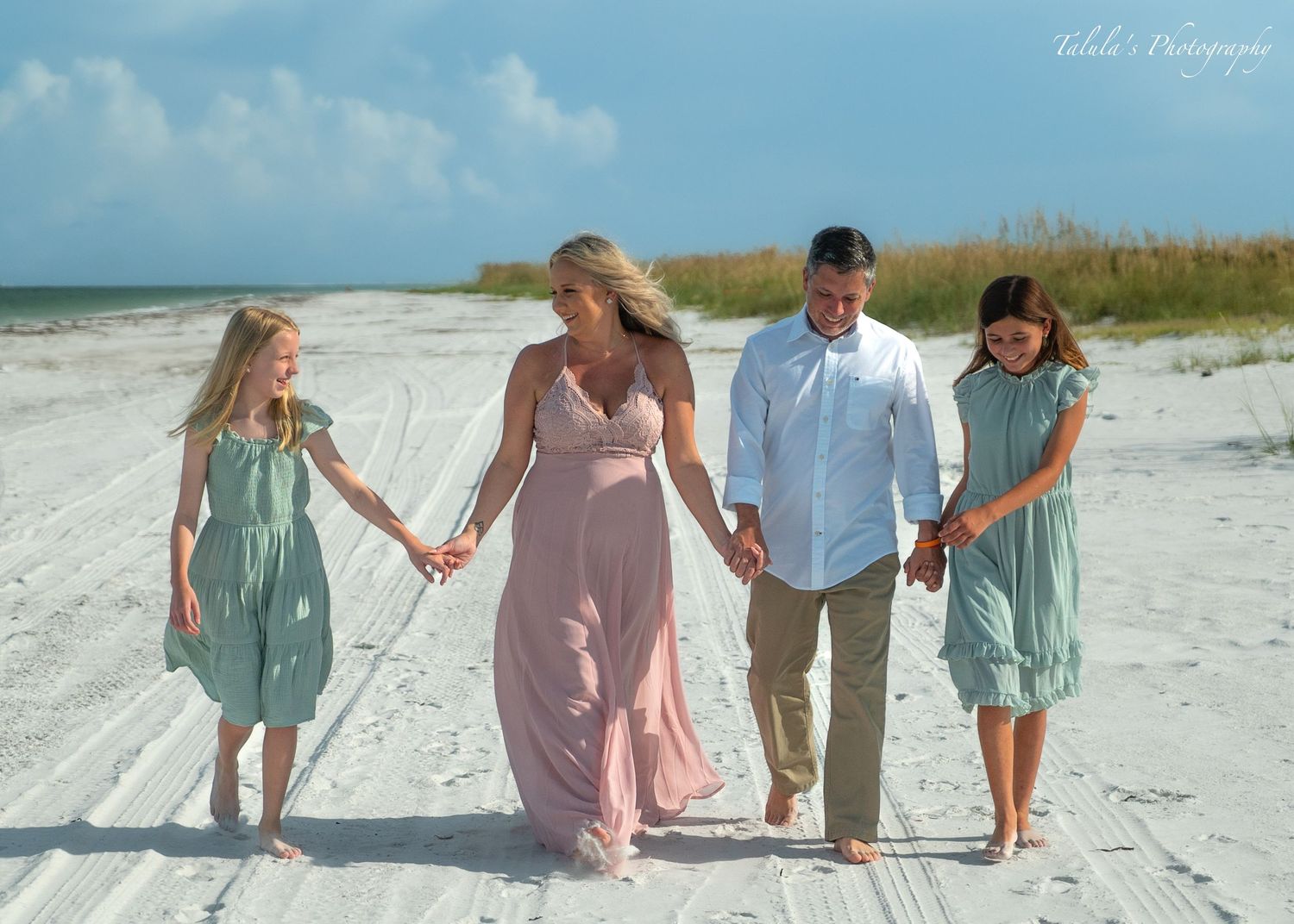 Family members sitting together on white sand beach holding hands.