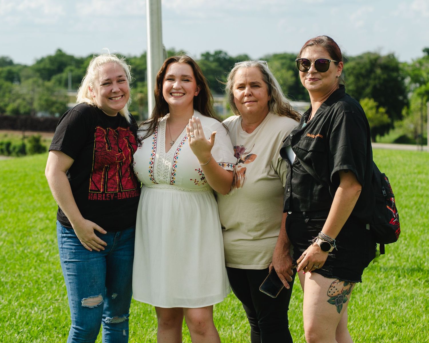 Group of four people posing together on grassy hill during outdoor gathering.