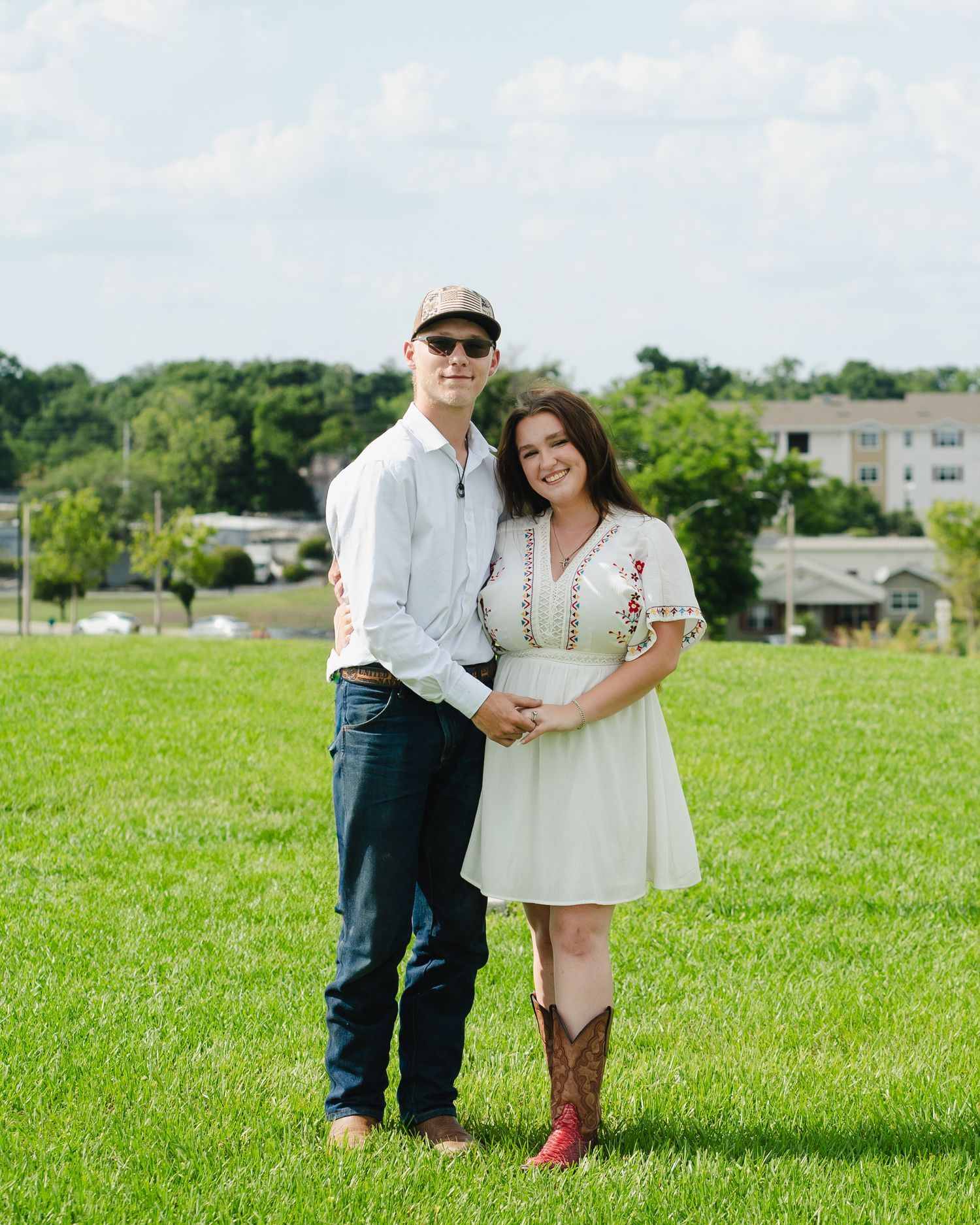 People stand together in a grassy field with buildings visible in the background.