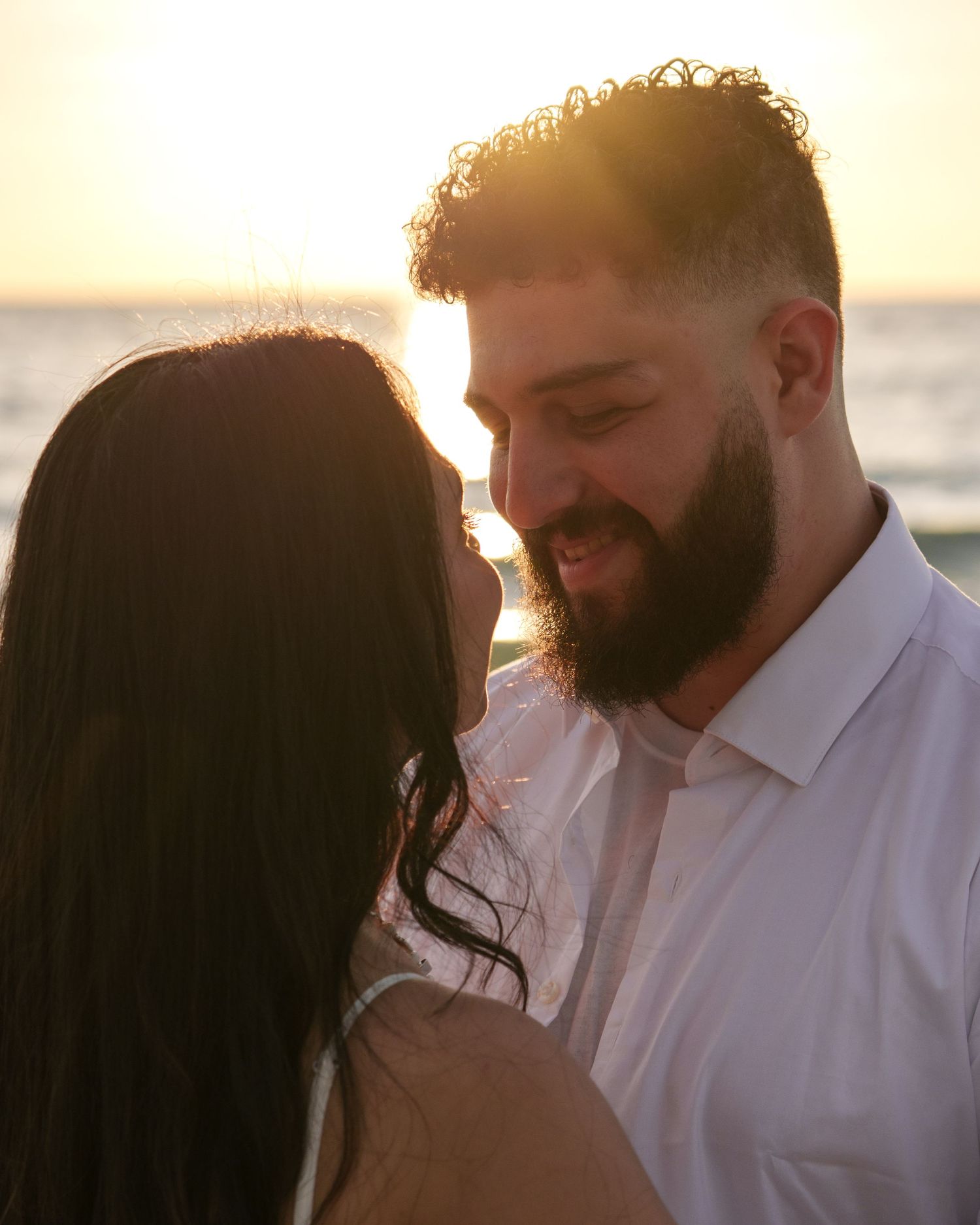 Romantic beach photoshoot at golden hour with couple in white outfits.