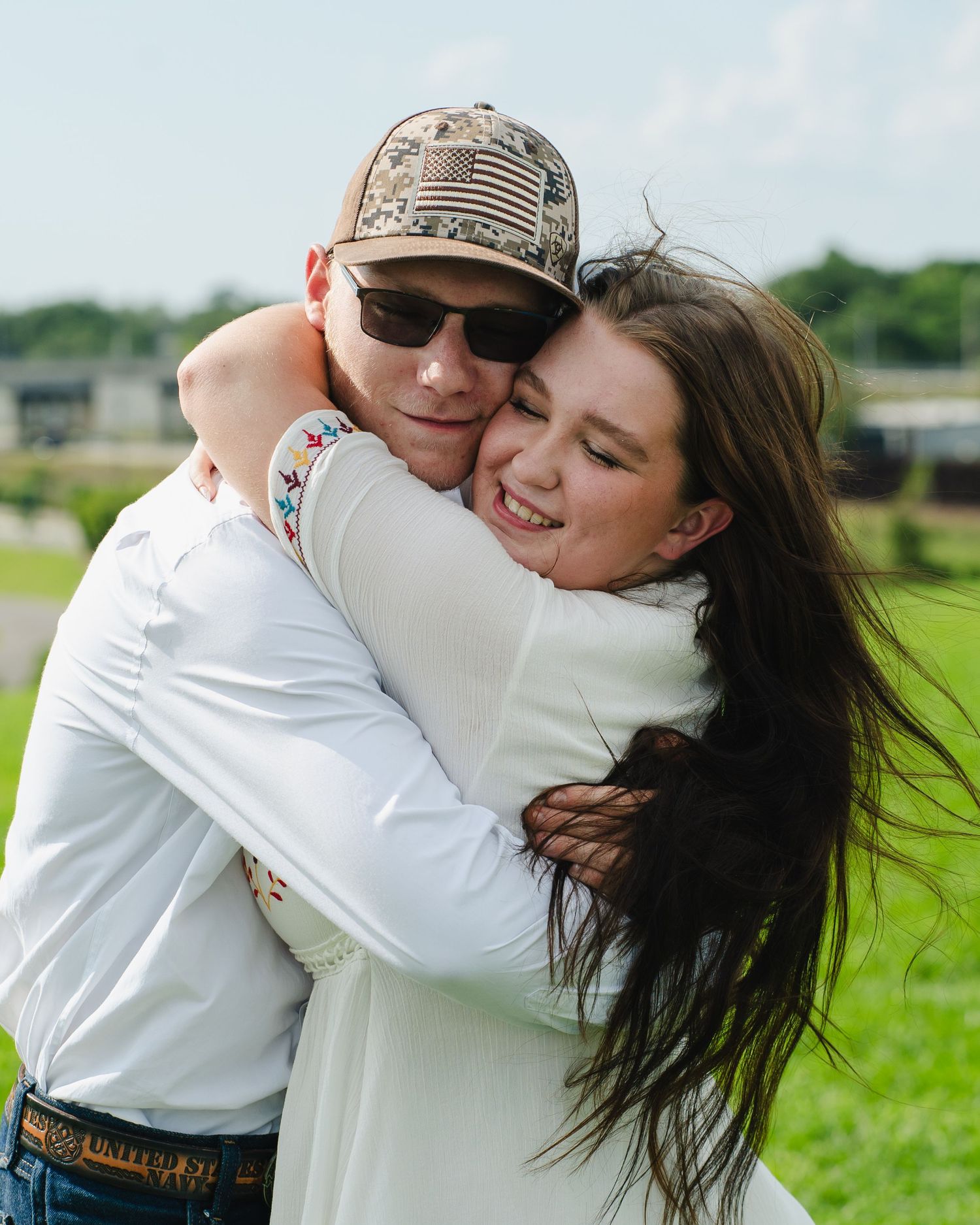 Two people share an emotional embrace in a sunlit meadow.