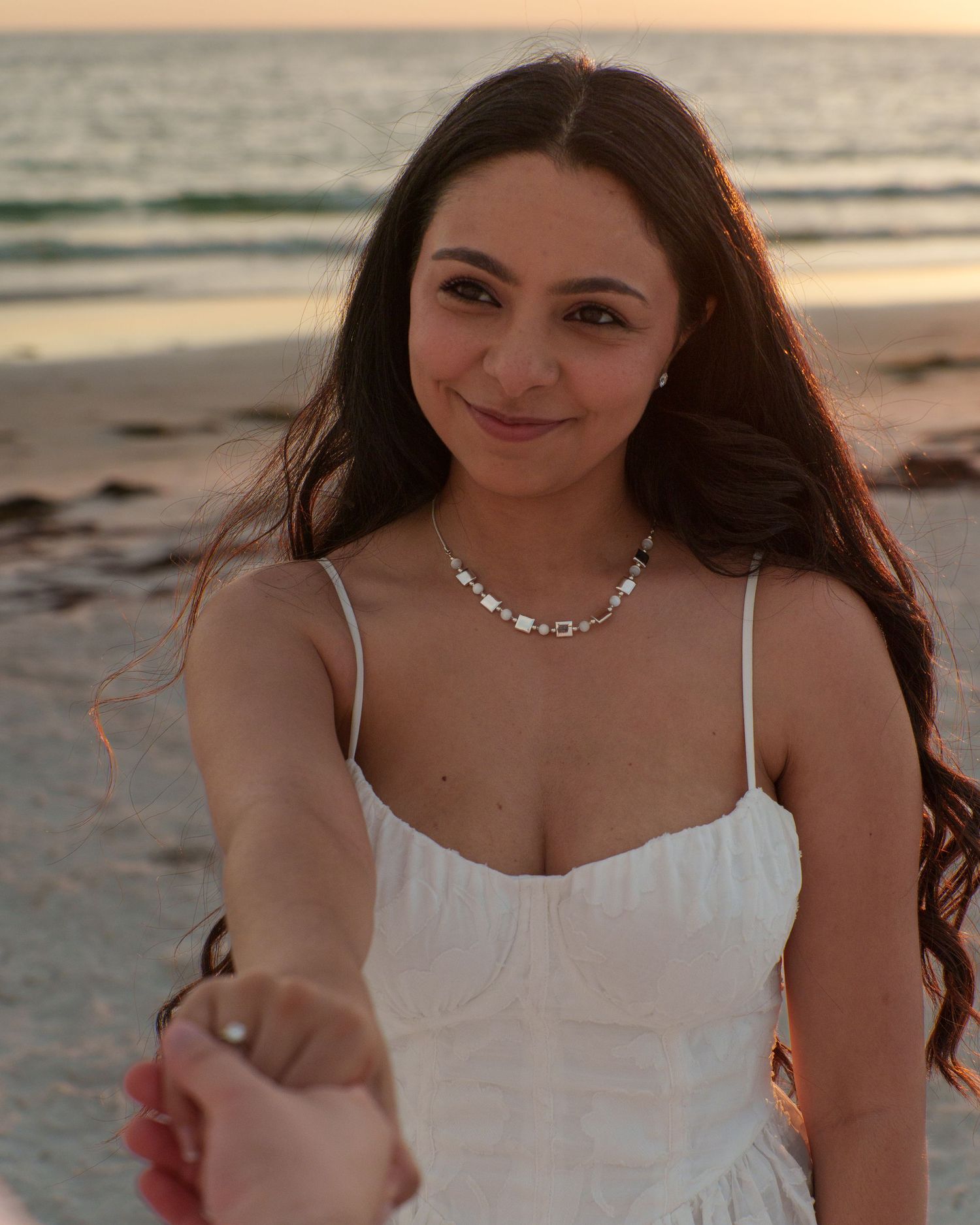 Woman in white dress smiling during beach photoshoot at sunset.