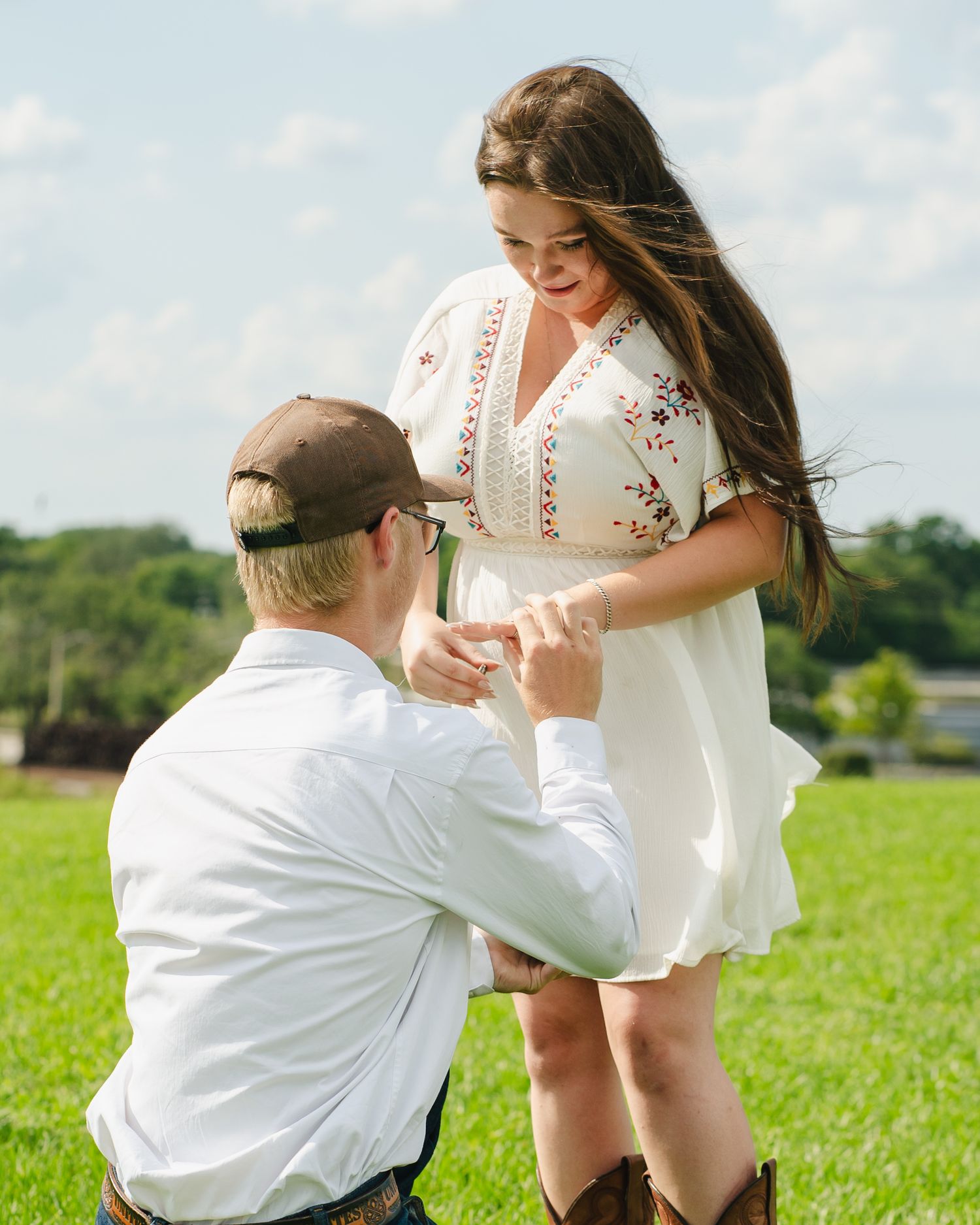 A couple shares a tender moment in a grassy field during what appears to be a proposal.