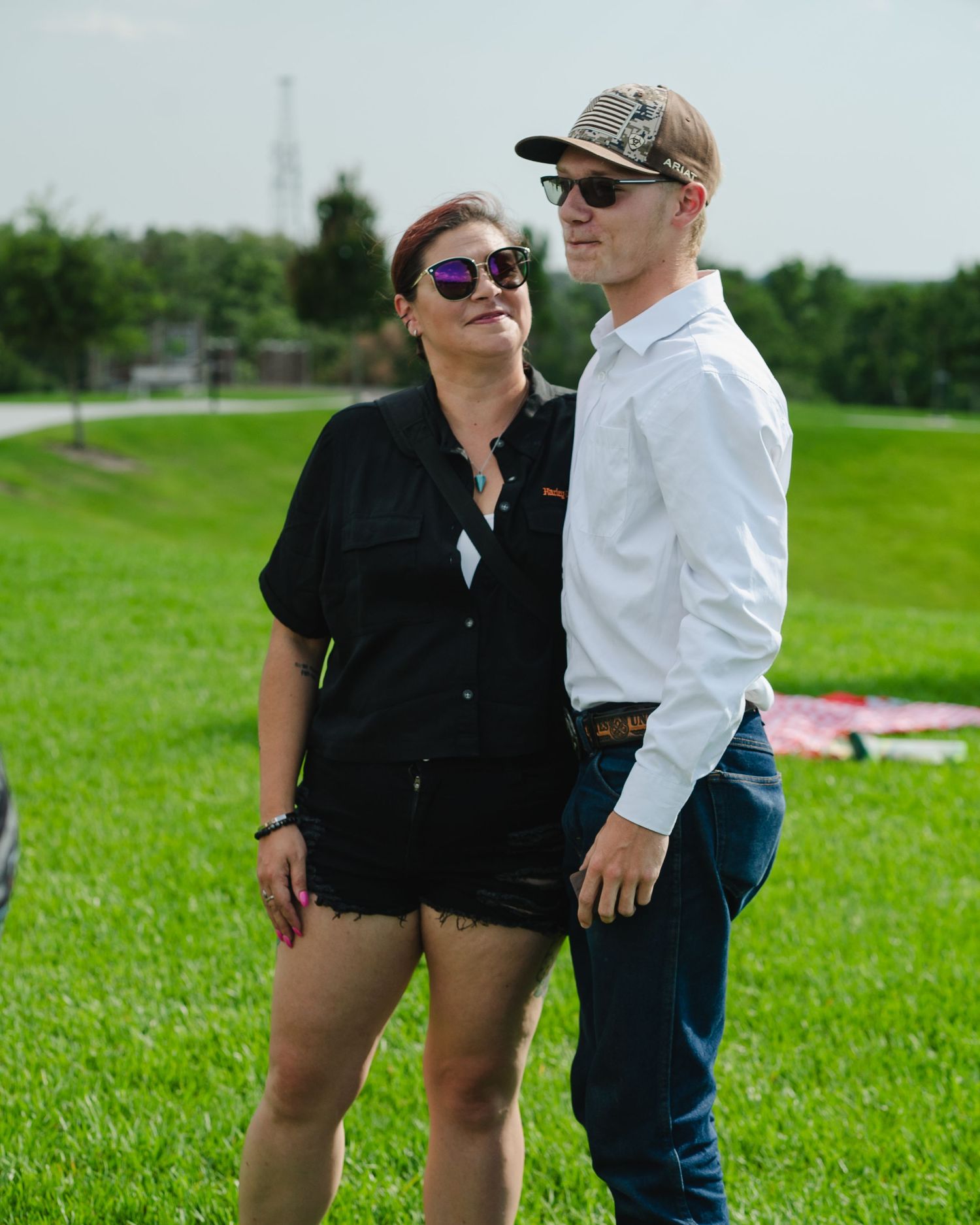 Two people in casual summer attire standing together on green grass.
