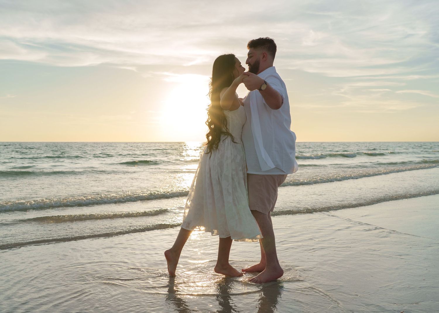 A couple walking and dancing together on a sandy beach at sunset.