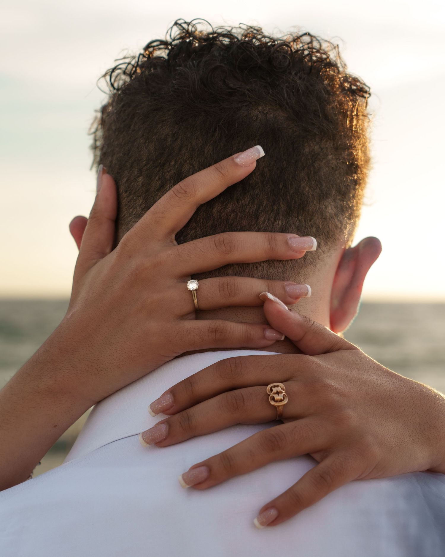 Close-up of hands with rings resting on a white shirt during a beach photoshoot.