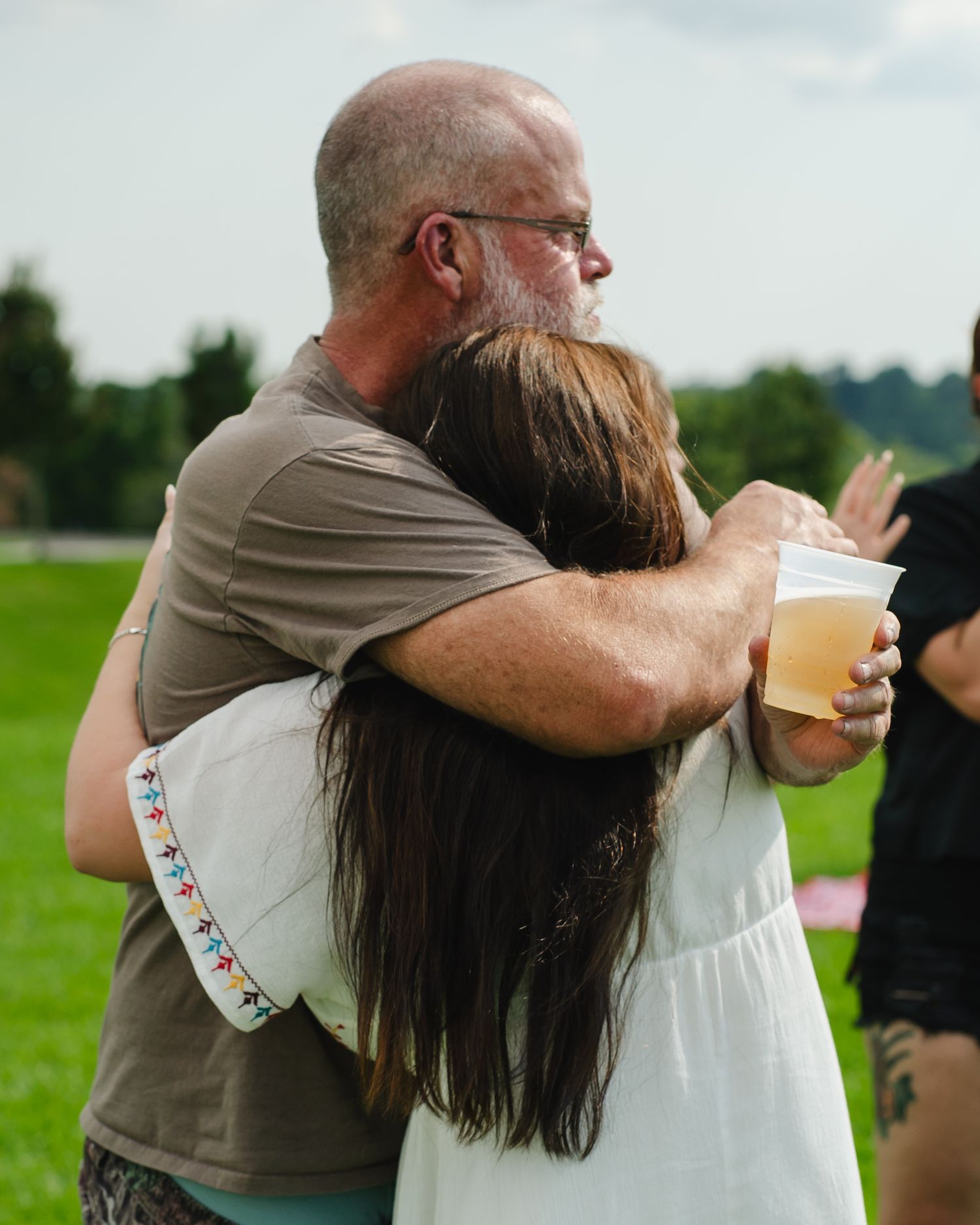 An emotional embrace is shared between two people in a sunny field.