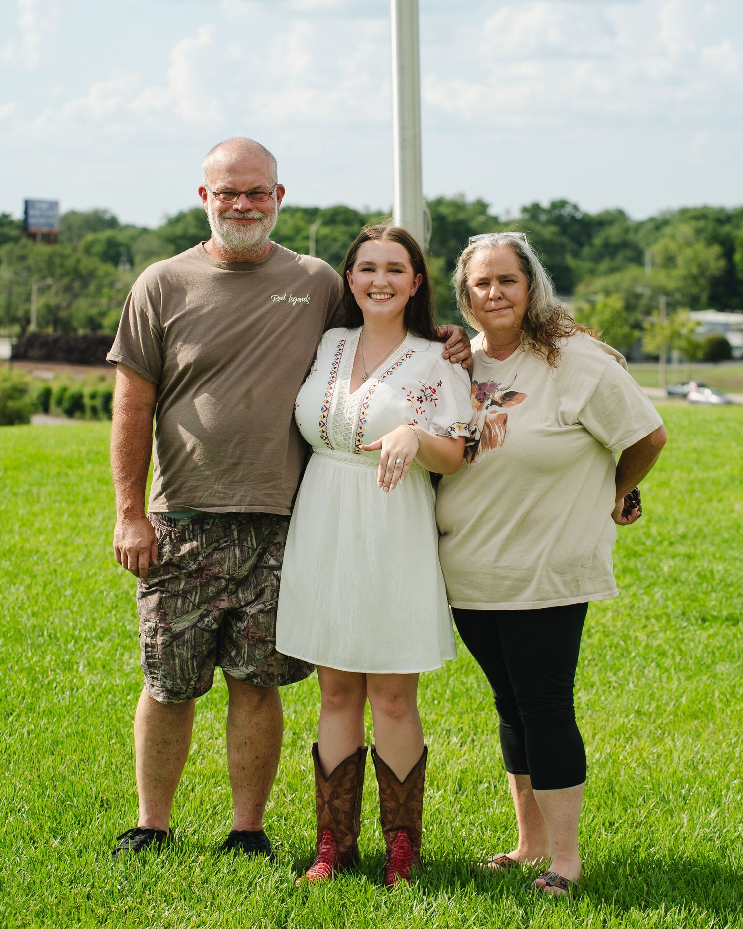 Three people pose together on grassy hill with white pole in background.