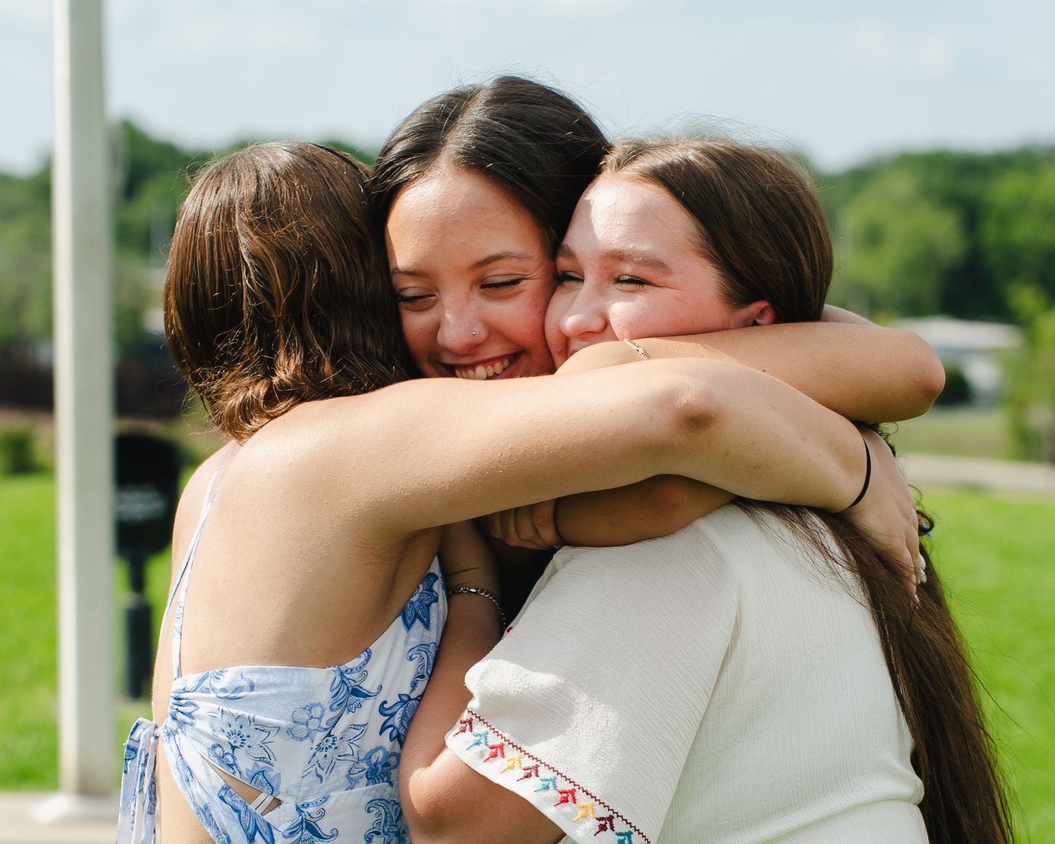 Friends share a group hug outdoors in summer attire.