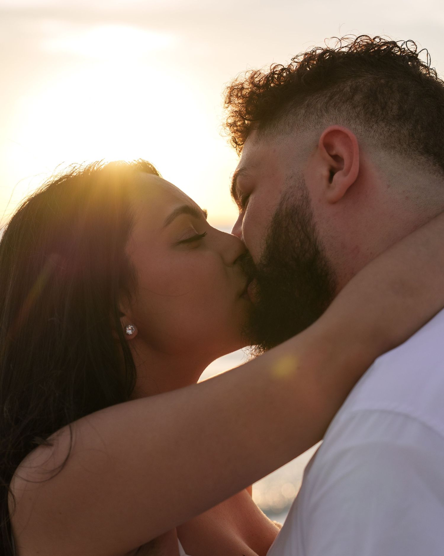 Silhouetted couple sharing romantic kiss on beach during sunset.