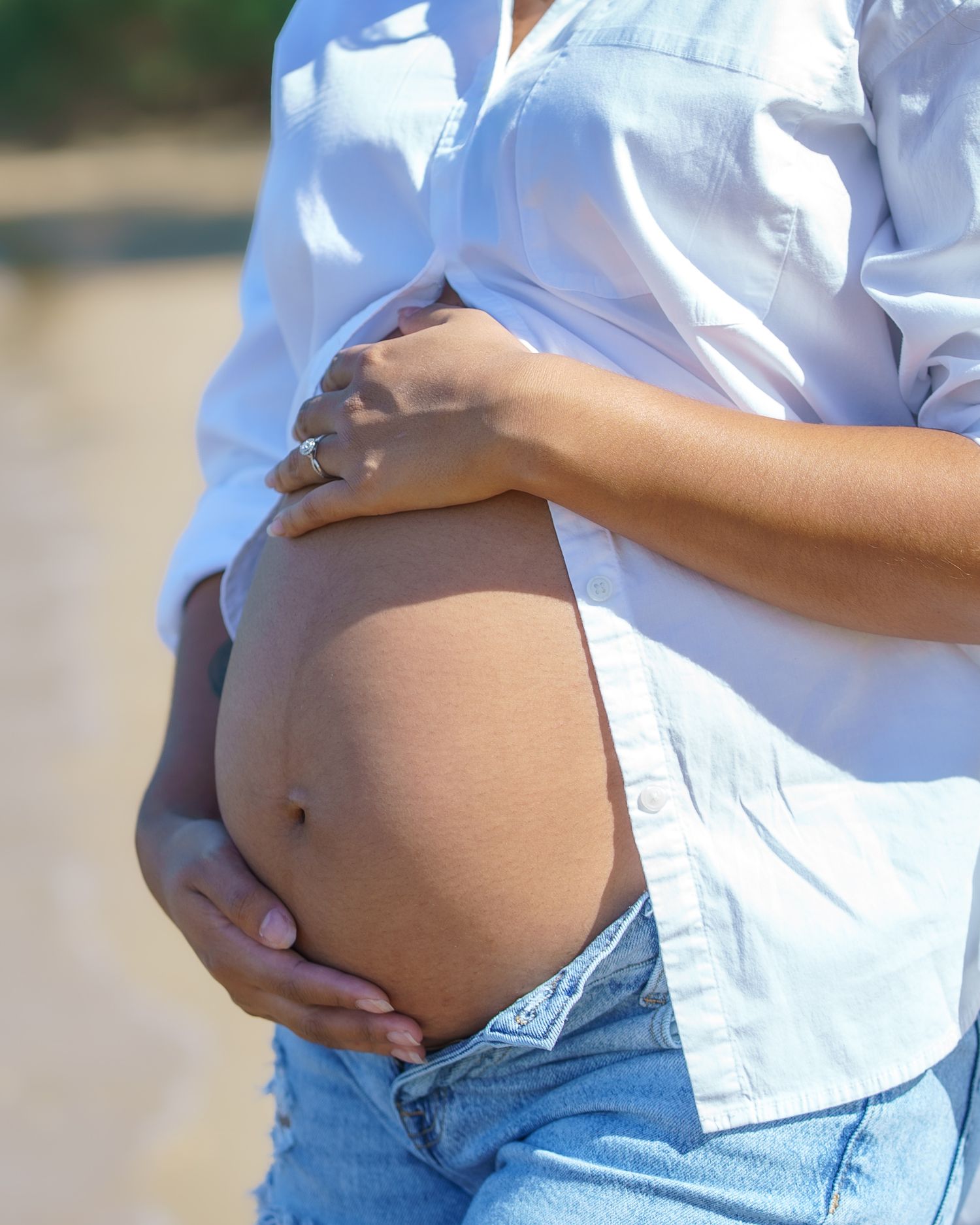 Close-up shots of a pregnant belly in a white button-down shirt and jeans.