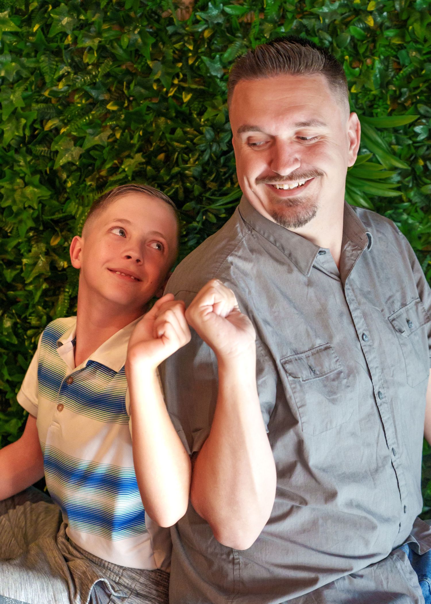 Two people sitting together against a green leafy background outdoors.