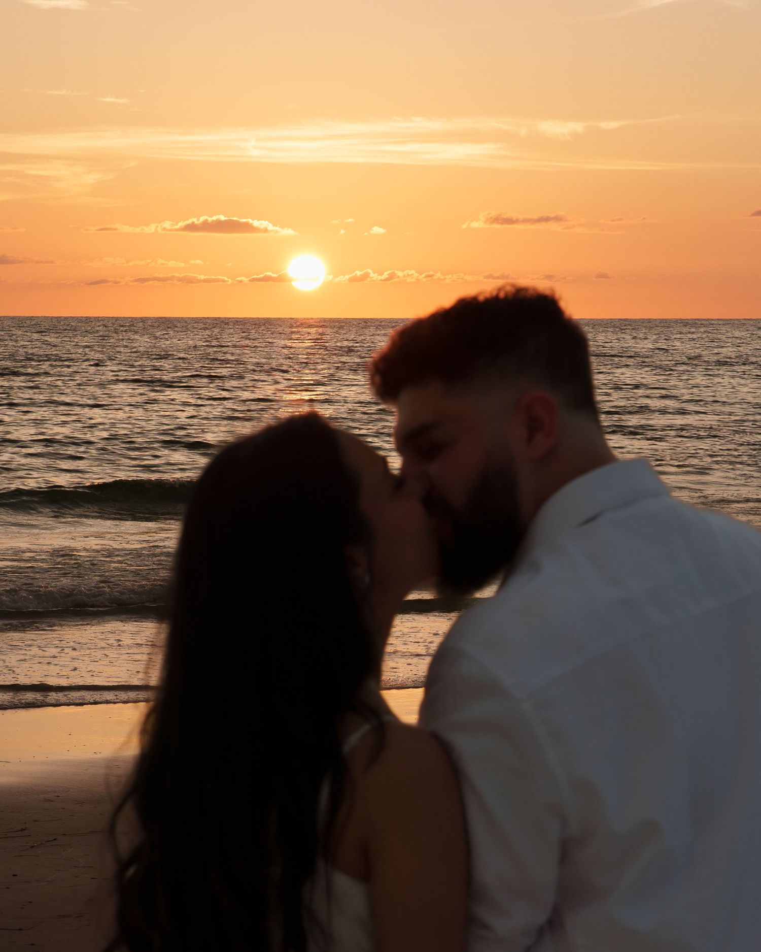 A silhouetted couple shares a tender moment during a golden sunset by the ocean.