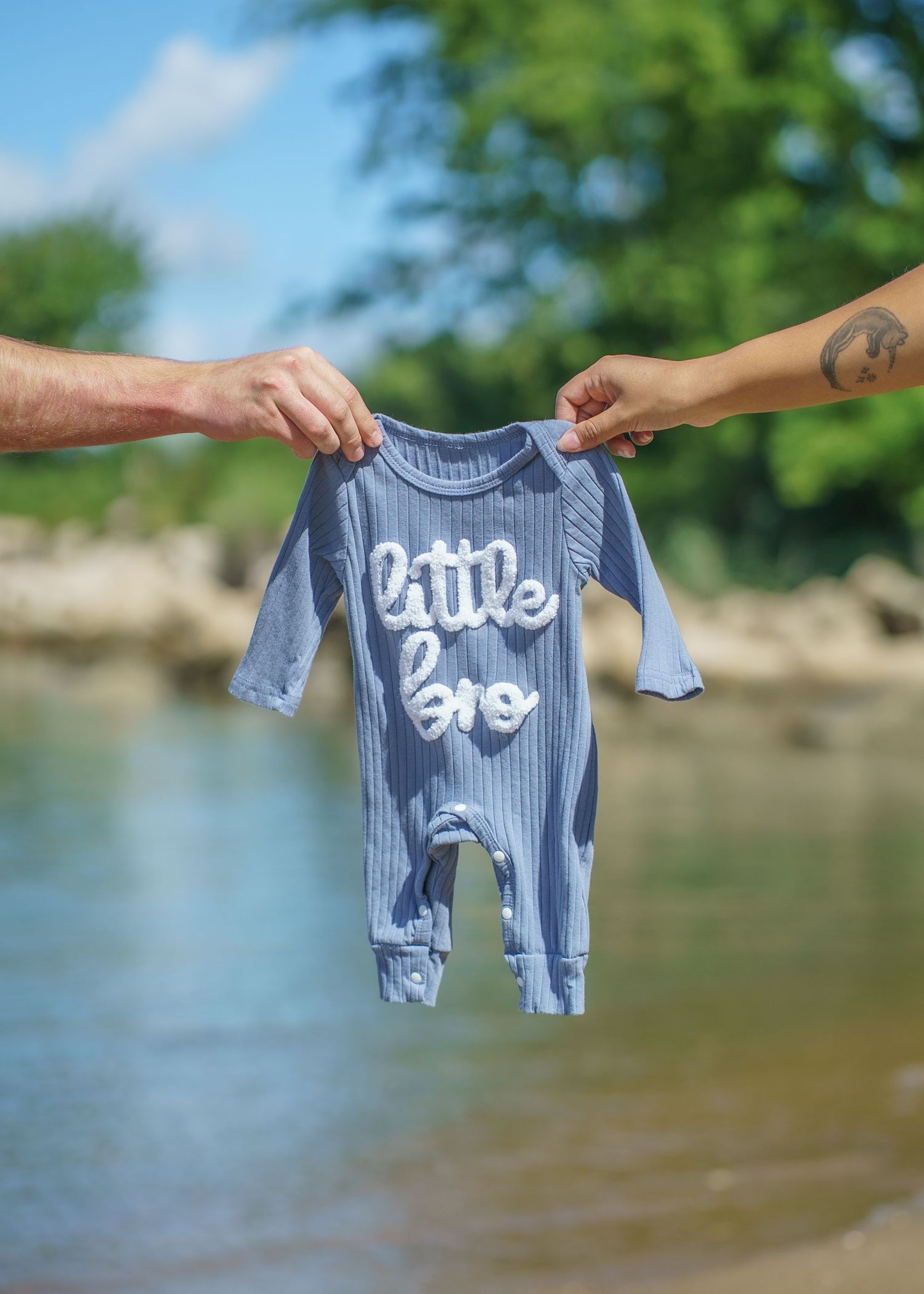 A small blue and white striped baby onesie being displayed near a lake.