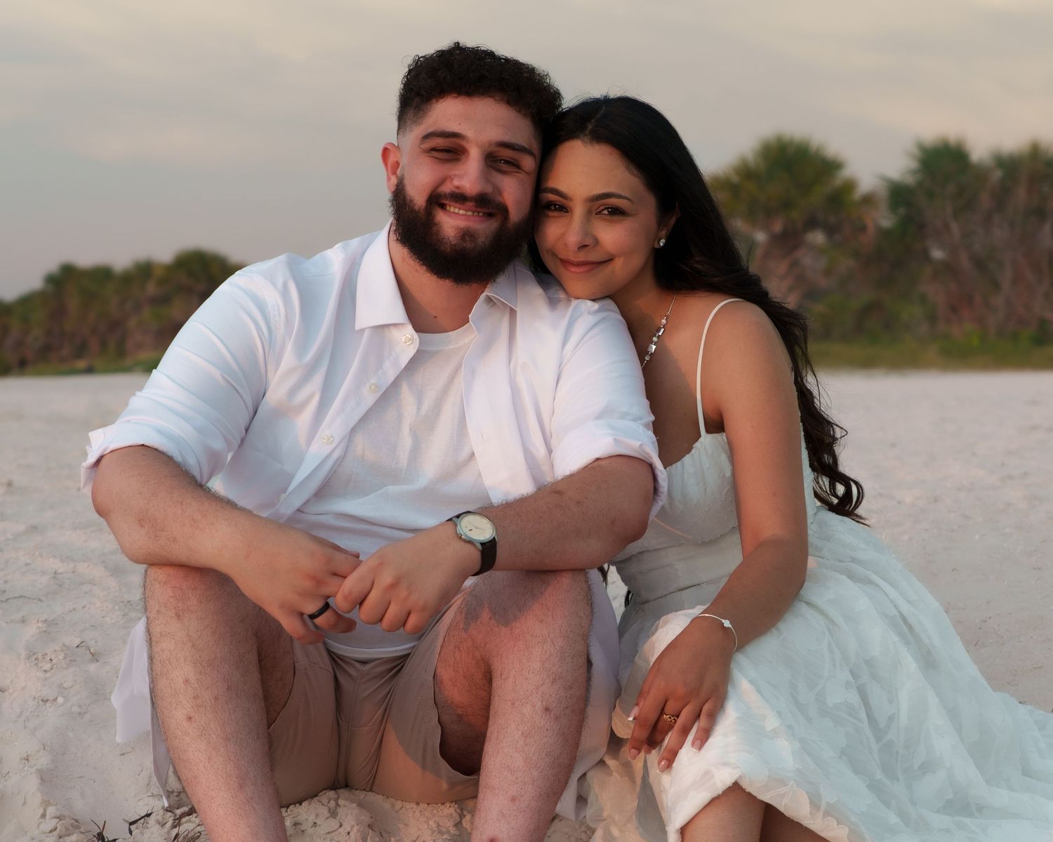 Couple relaxing together on sandy beach during sunset session.