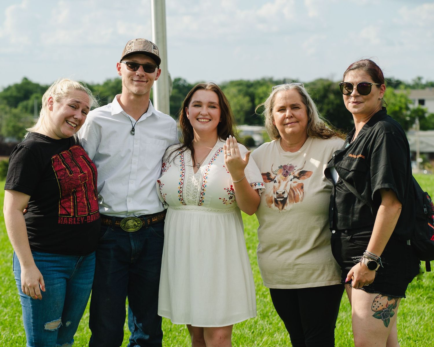 A group poses together for a photo on a sunny day in a green field.
