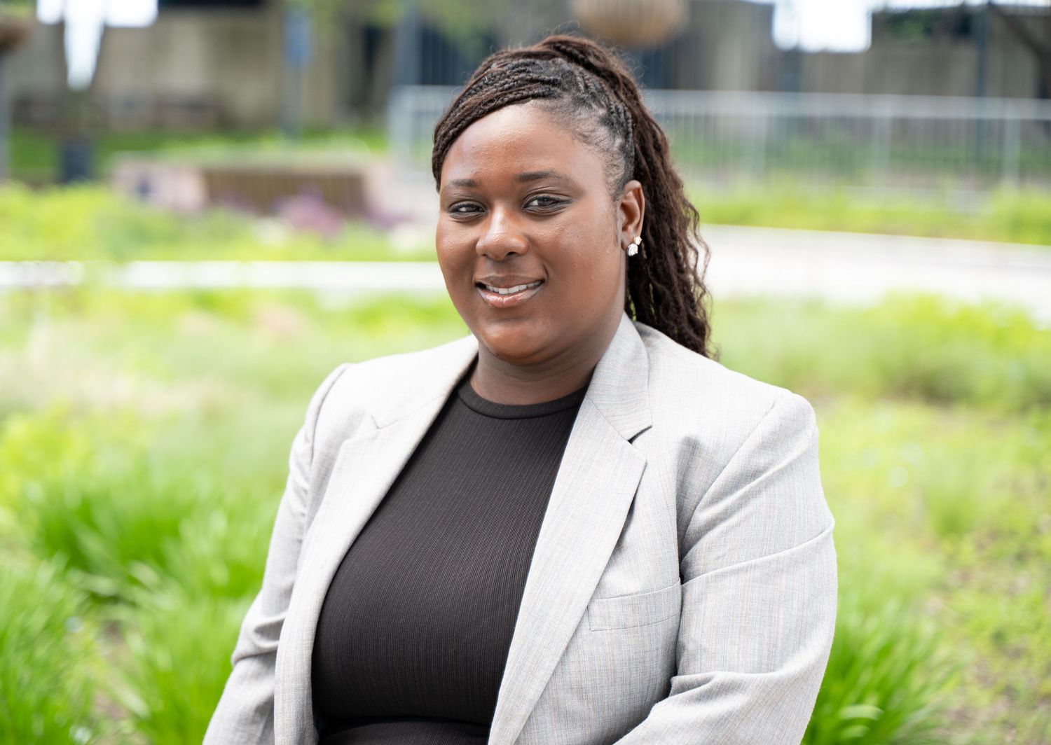 Person in business attire sitting outdoors on a bench surrounded by greenery.